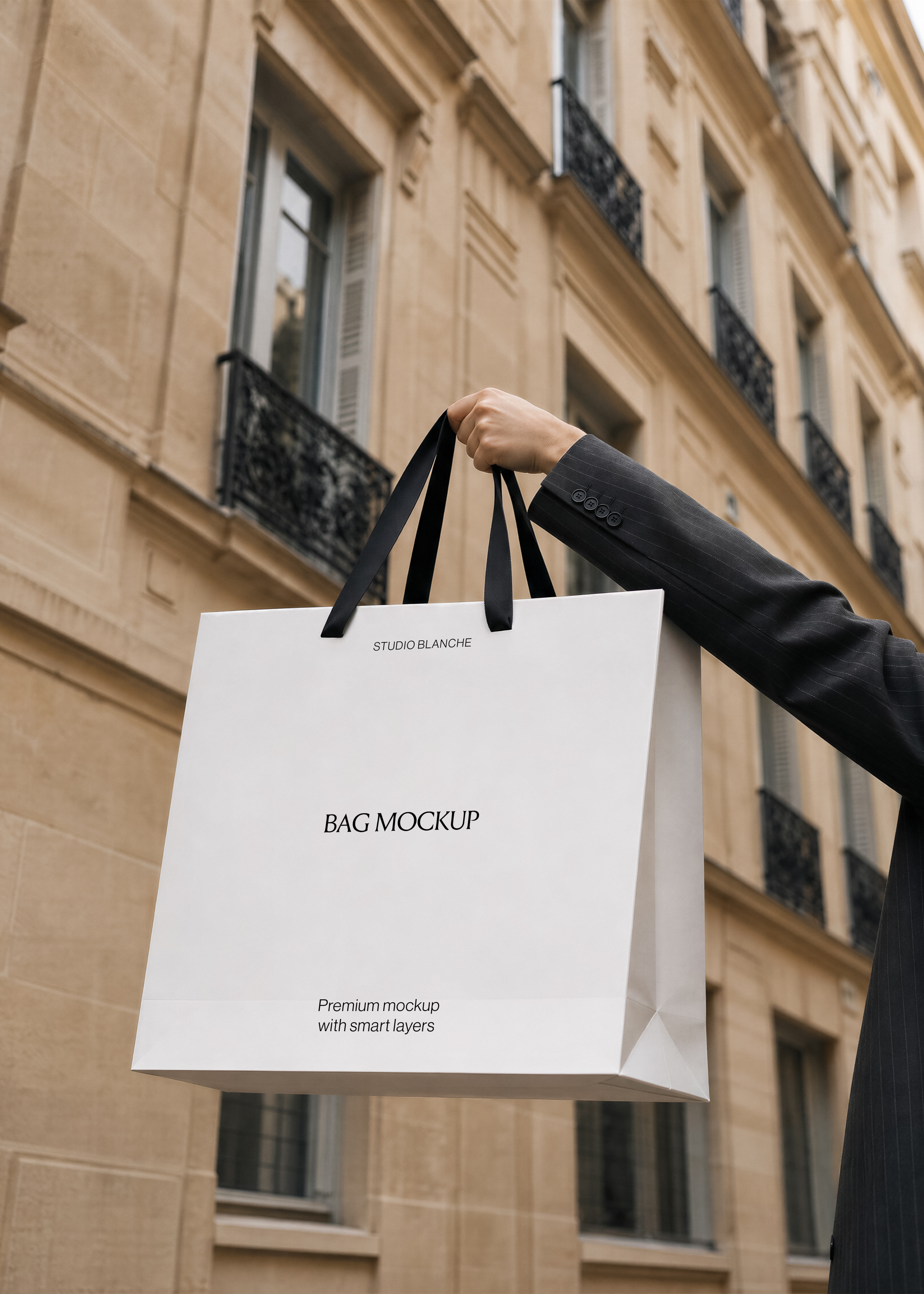 Studio Blanche shopping bag mockup with black ribbon handles held up against a sandstone Paris building with balconies