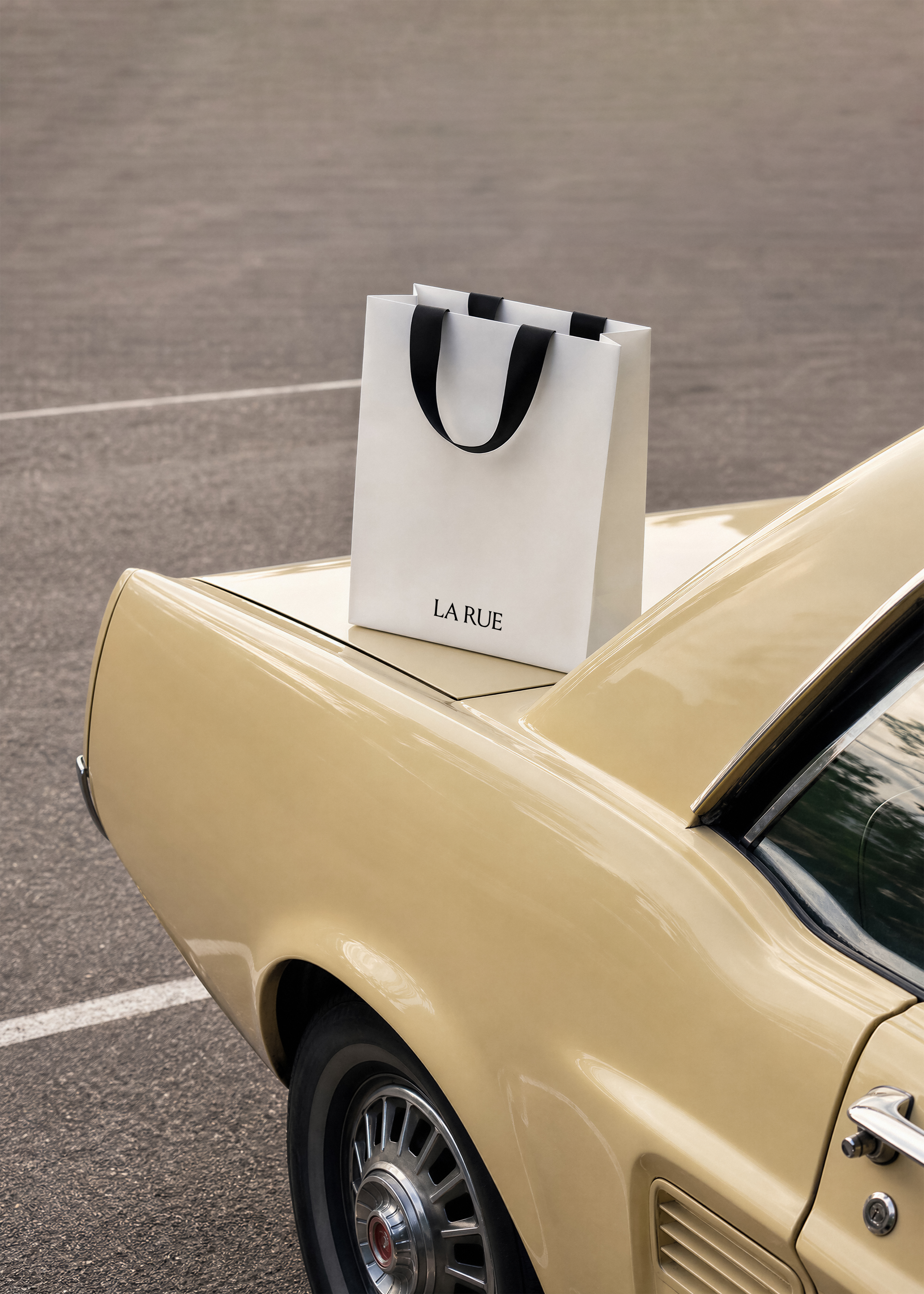 White LA RUE shopping bag with black ribbon handles standing on the cream boot of a vintage car in a car park