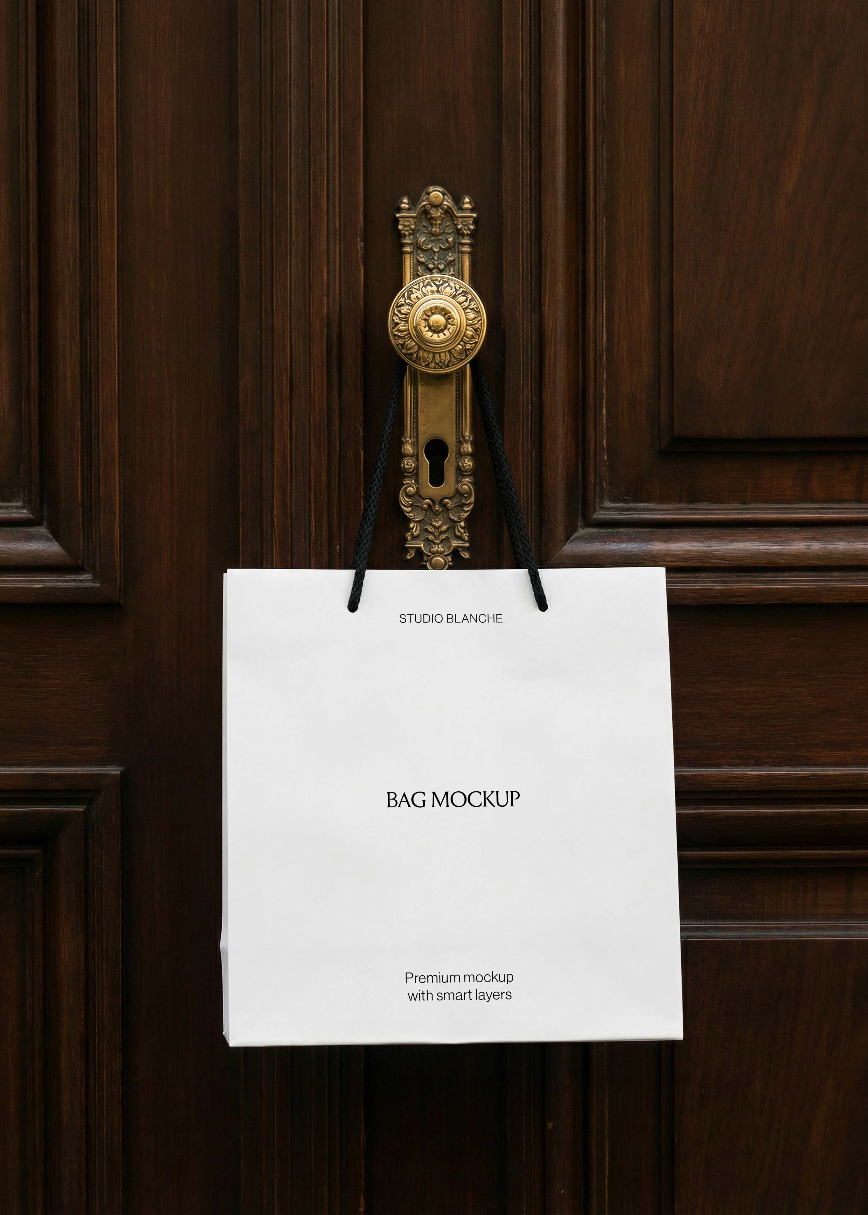 White paper bag mockup with black rope handles on antique brass door handle, dark mahogany panelled door behind