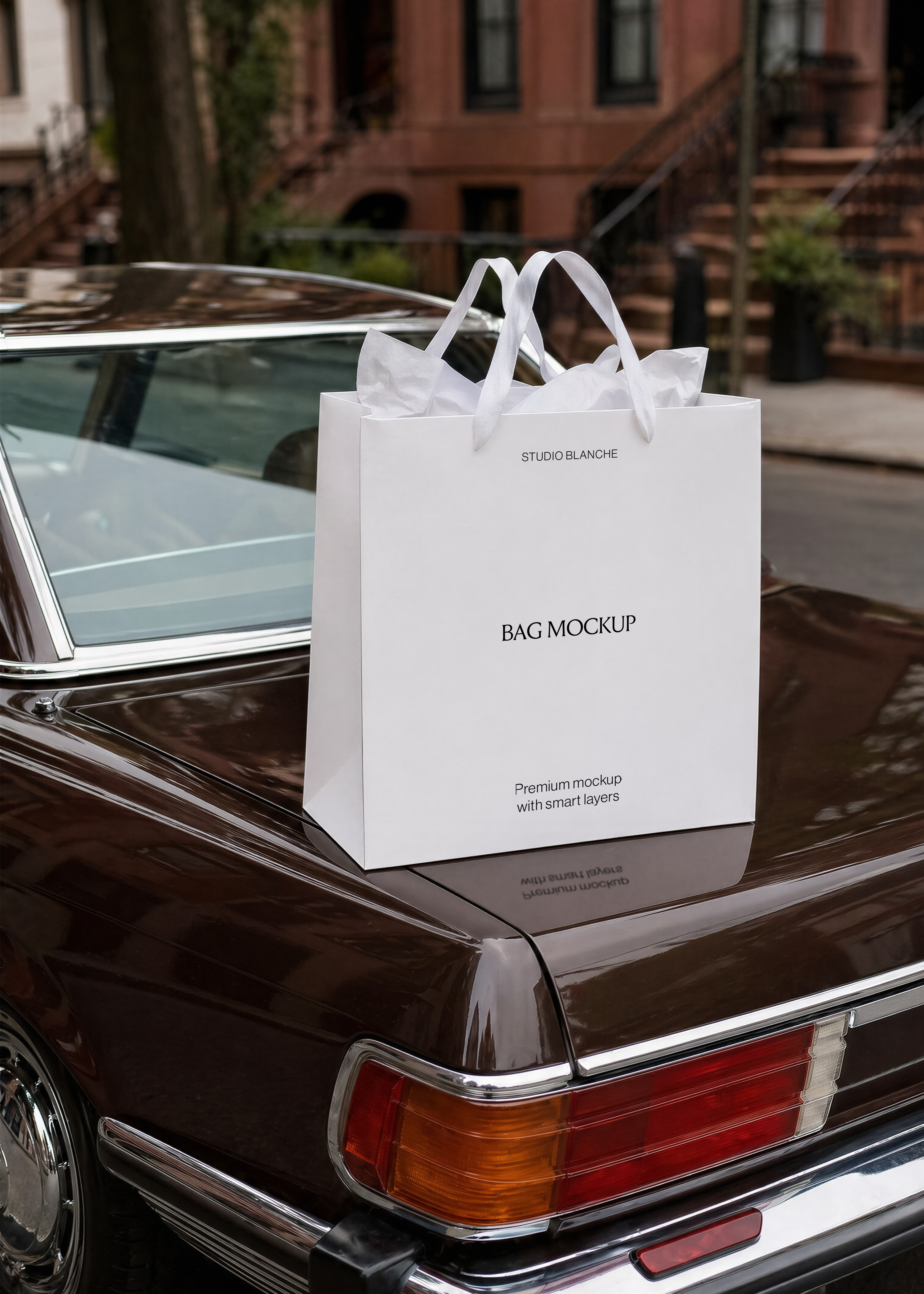 White shopping bag mockup with ribbon handles and tissue paper on vintage car boot, red tail light, brownstone steps