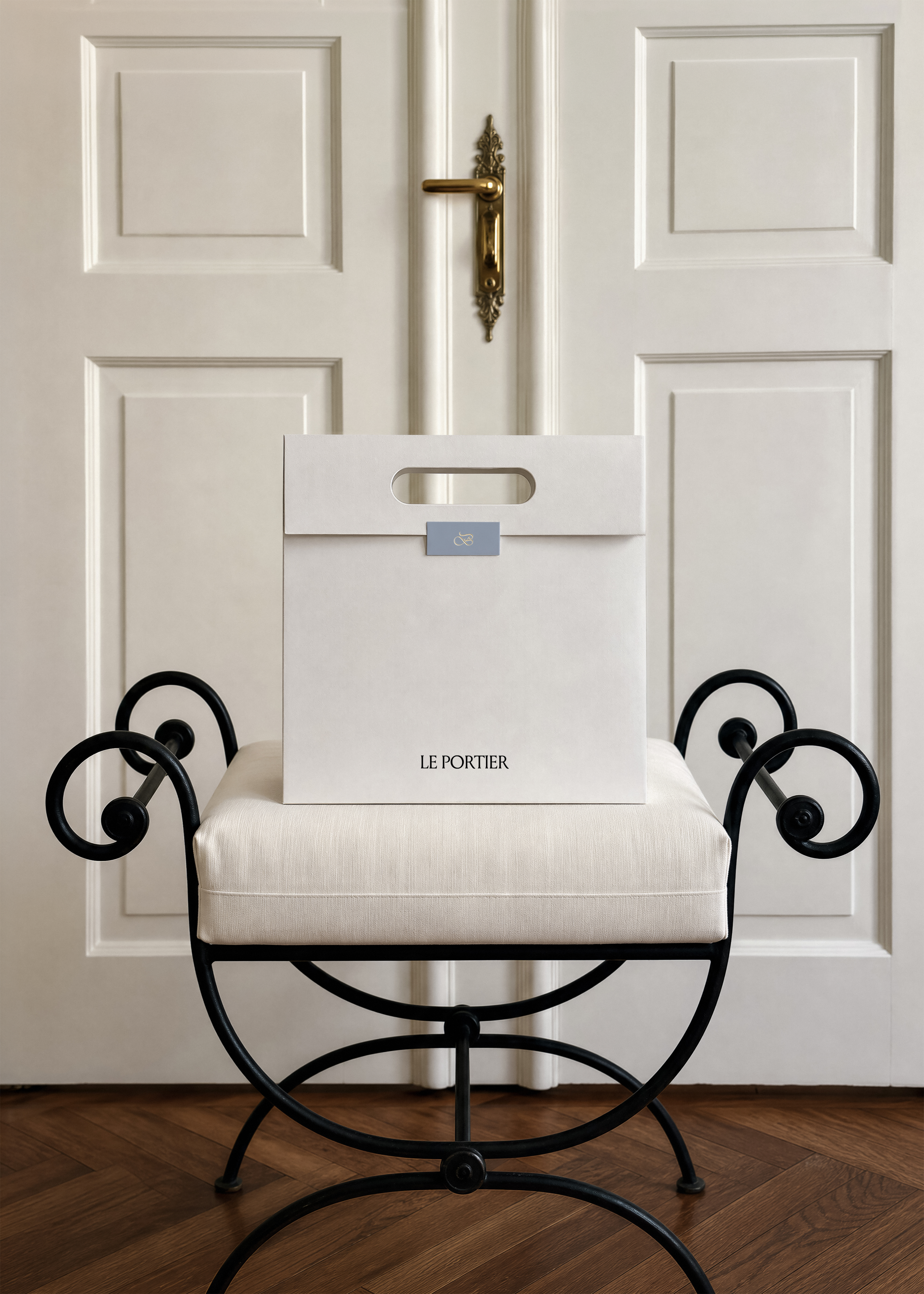Cream paper shopping bag mockup with blue swing label on a black wrought iron bench, panelled hotel door behind