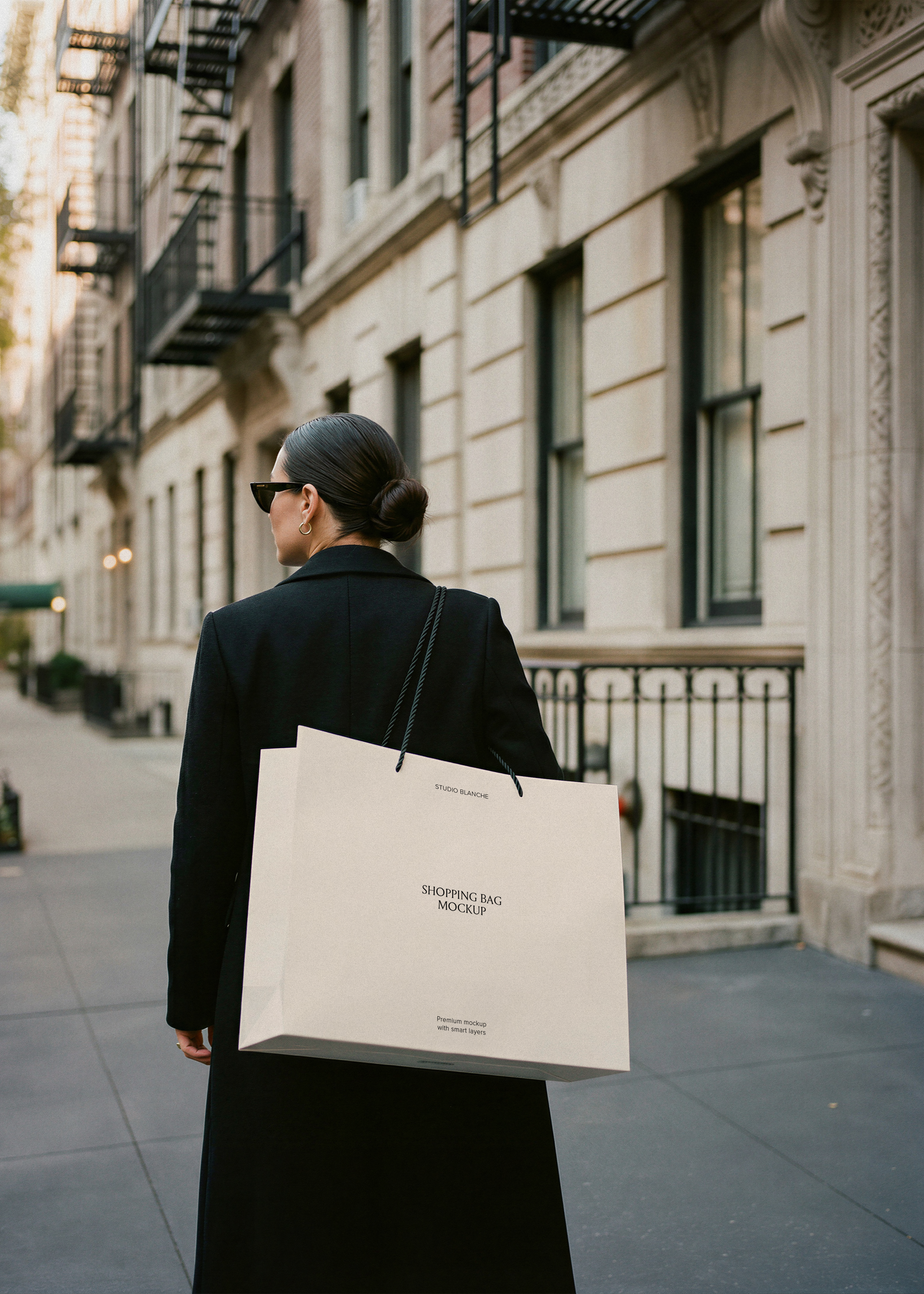 Woman in black coat carrying a blank cream luxury shopping bag with rope handles on a New York City street, from Studio Blanche