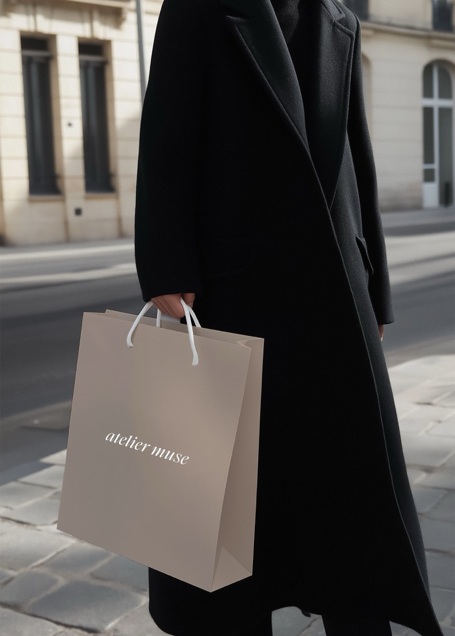 Person holding a 'atelier muse' shopping bag on a city street.