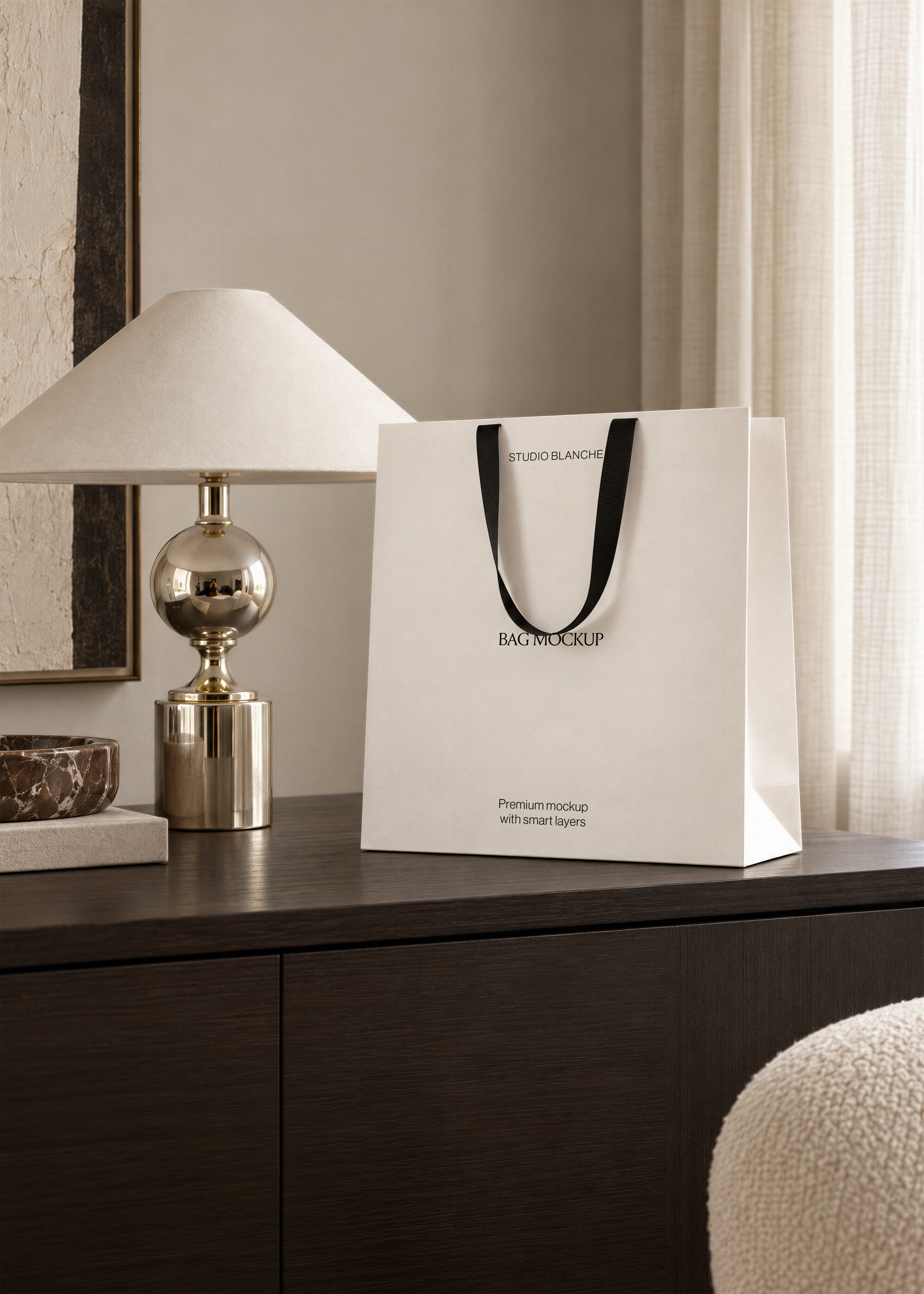 Shopping bag mockup with black ribbon handles on dark oak sideboard beside brass lamp and marble bowl, office interior