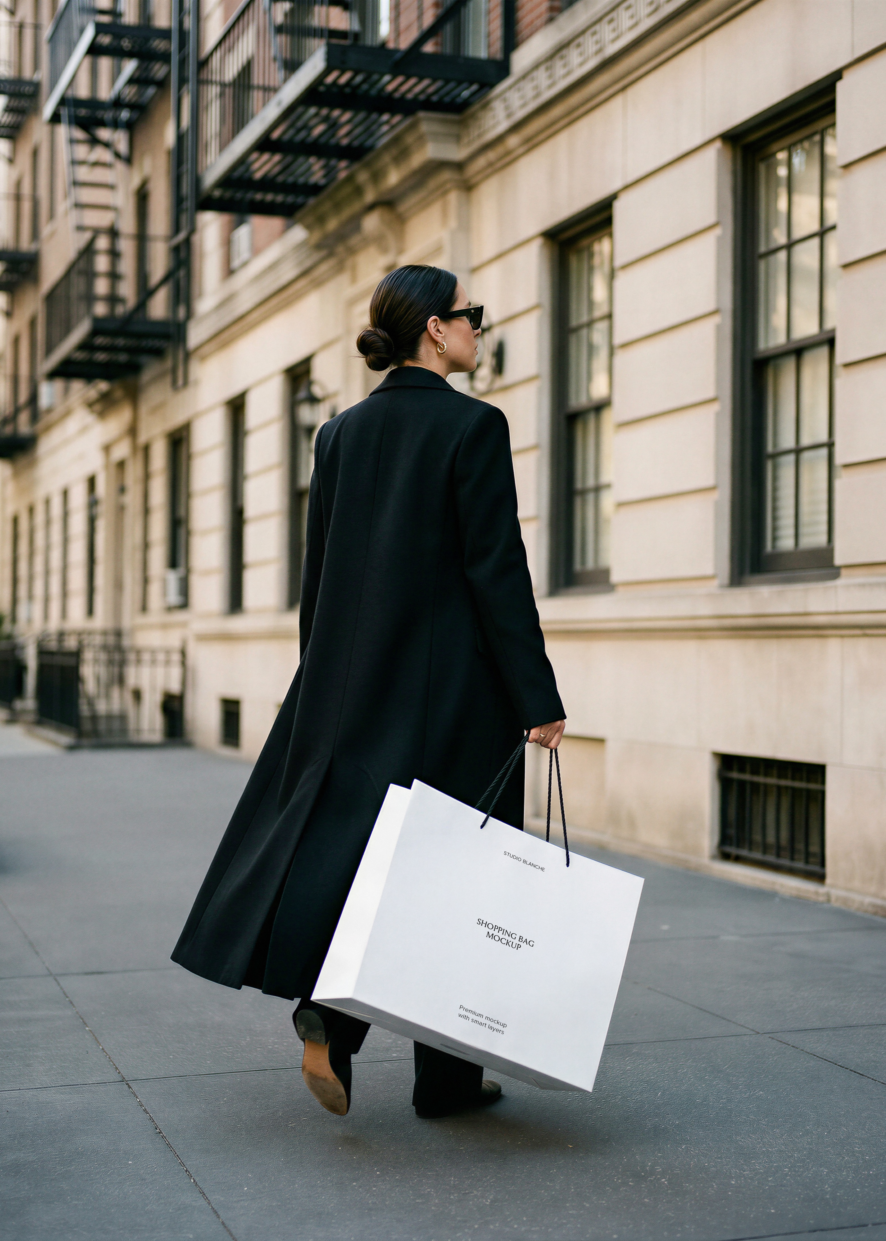 White shopping bag mockup with rope handles carried by woman in long black coat walking down a city street