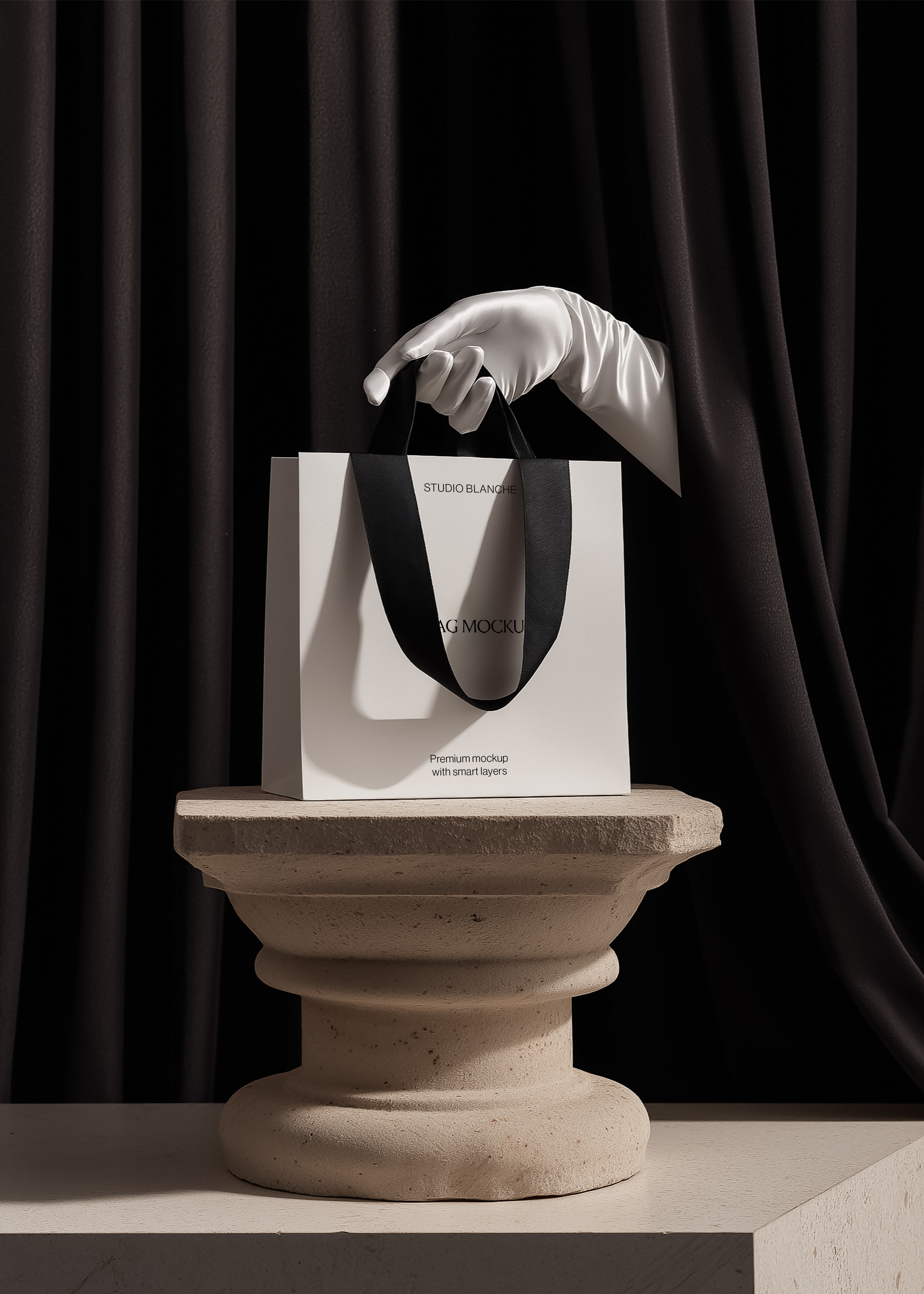 Luxury shopping bag mockup on textured stone pedestal, white satin gloved hand lifting handles, monochrome styling, black curtain background