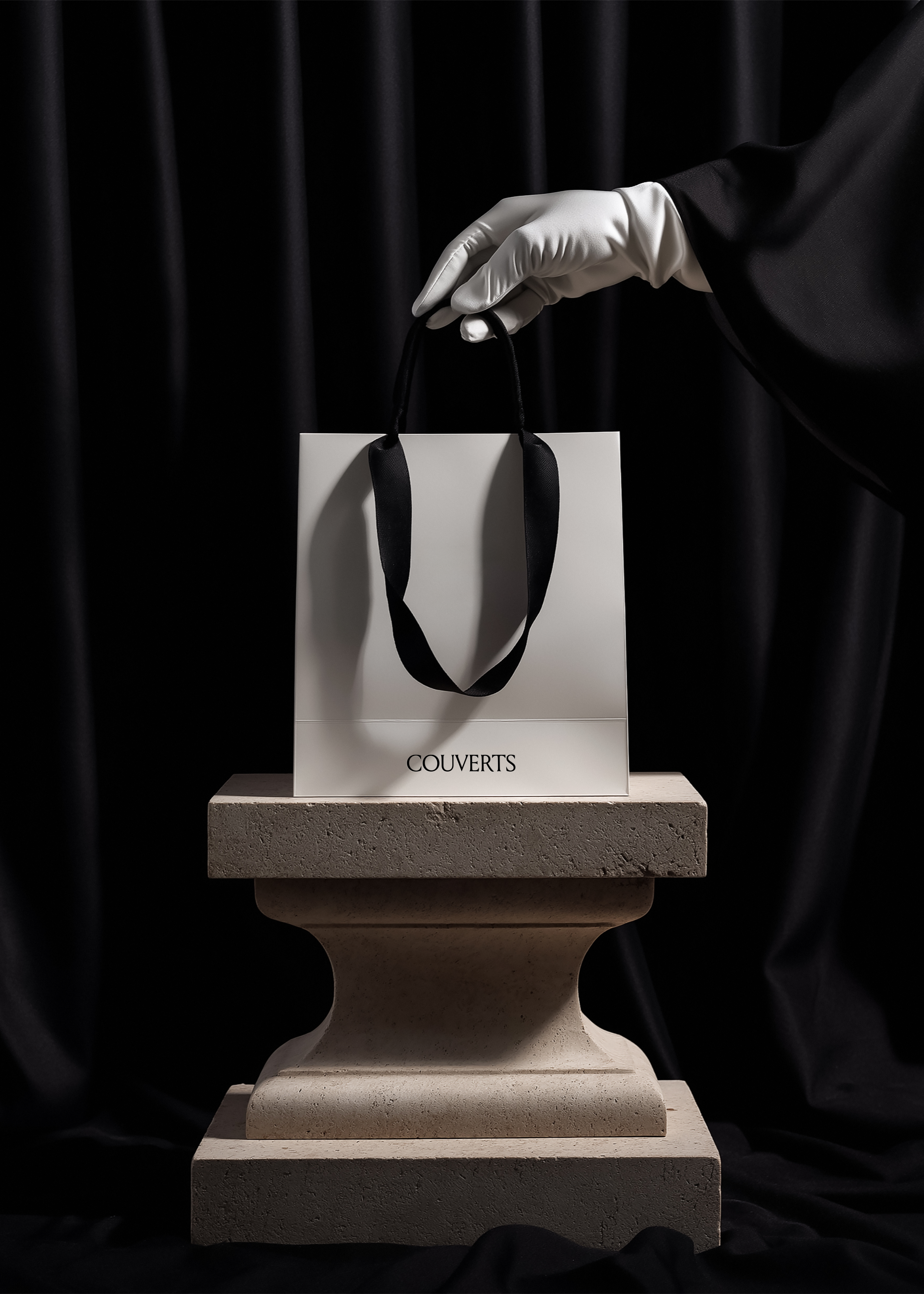 White paper shopping bag with black rope handles suspended by white satin-gloved hand above tiered travertine plinth, black draped curtain background