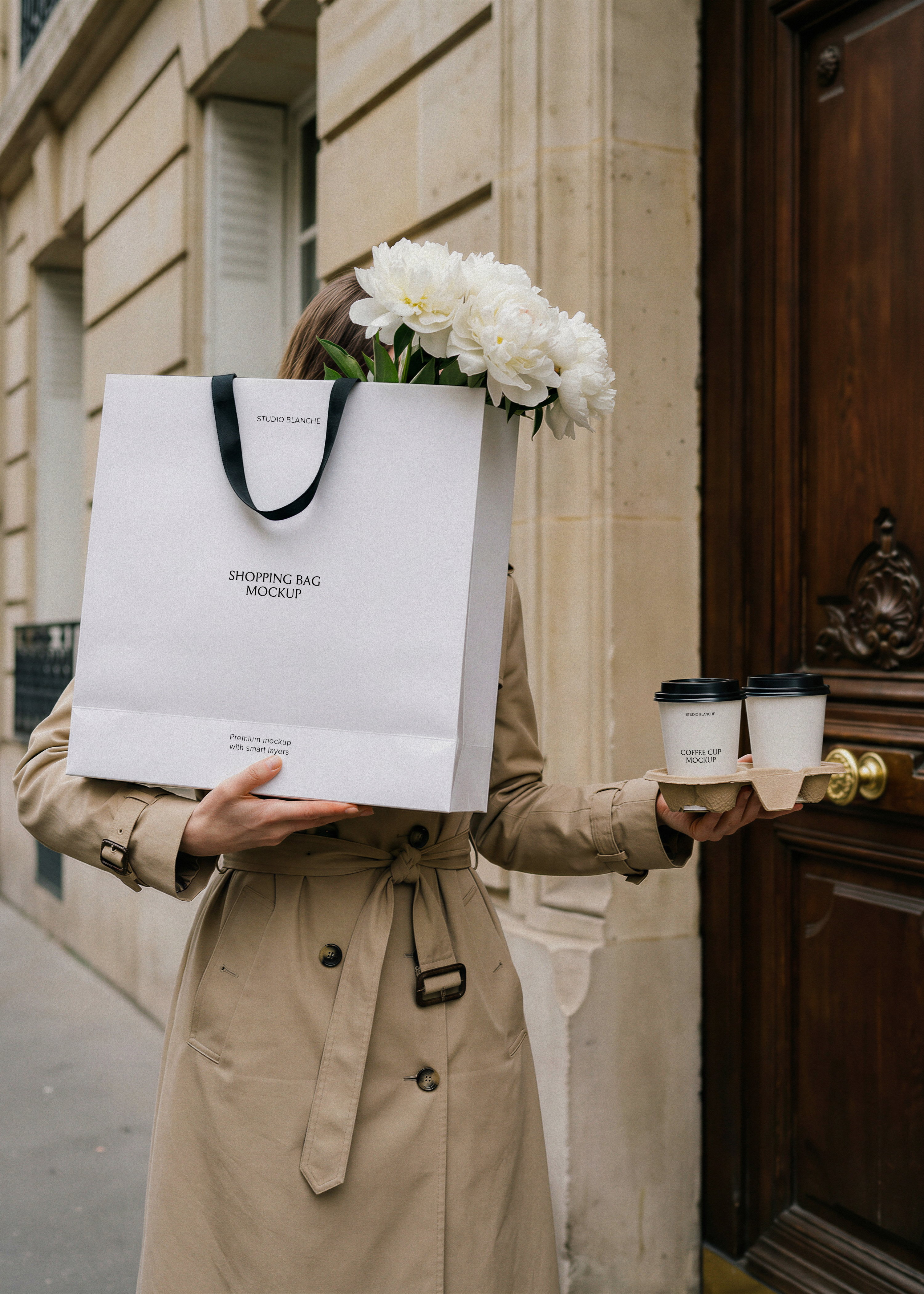 Shopping bag mockup held by woman in trench coat with white peonies and two takeaway coffee cups on Parisian street