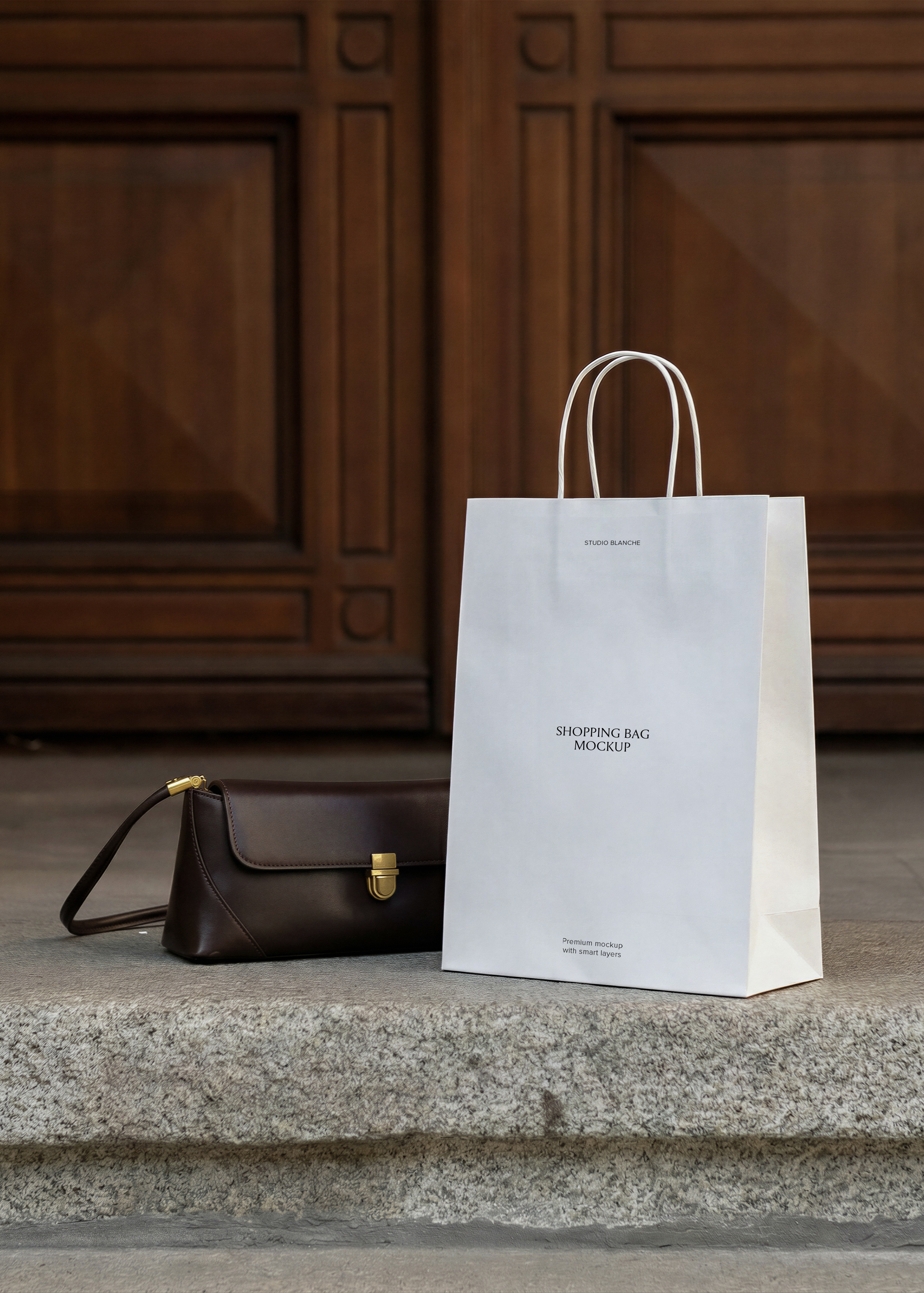 White paper shopping bag mockup with twisted handles styled with leather handbag on stone threshold and panelled timber door