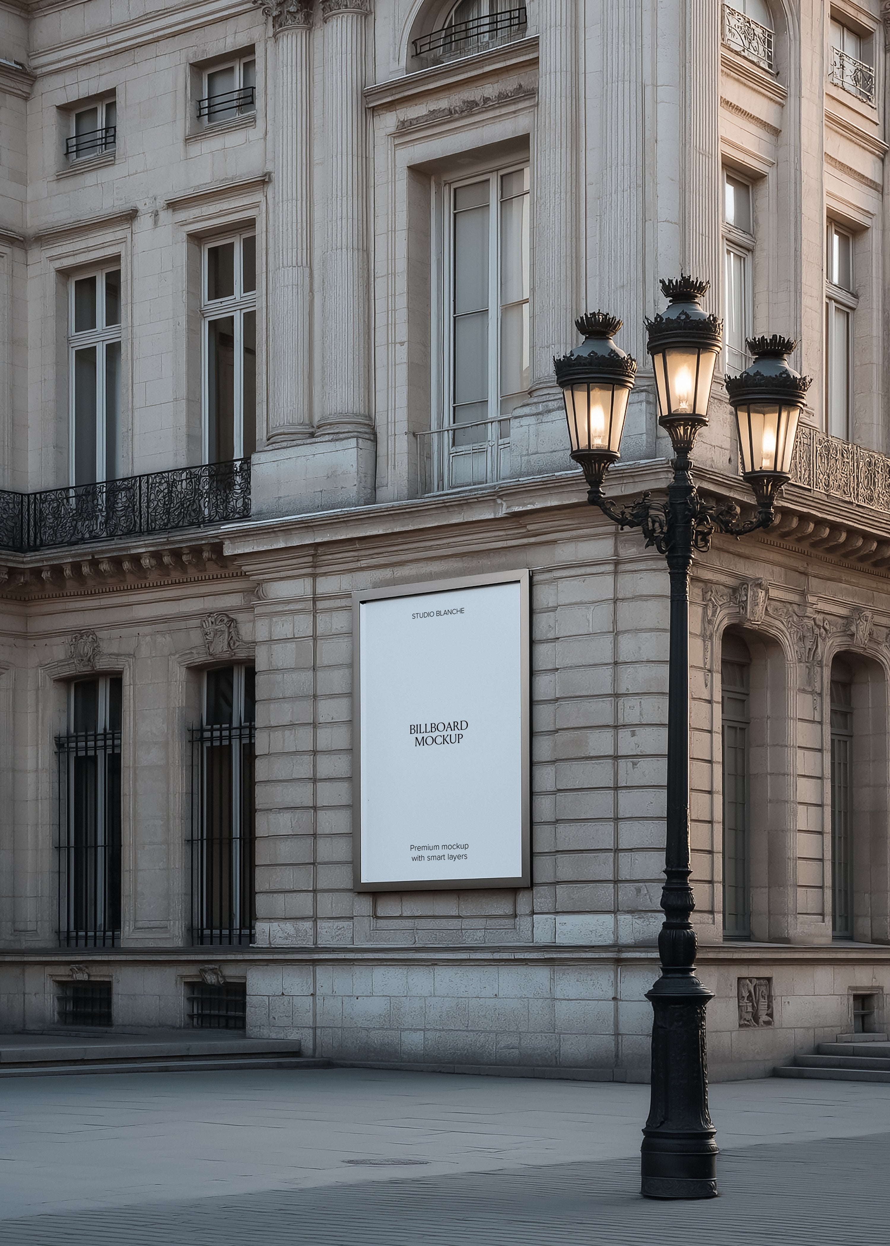 Blank billboard mockup on a Parisian corner facade at dusk, lamp post, empty white panel with Studio Blanche label