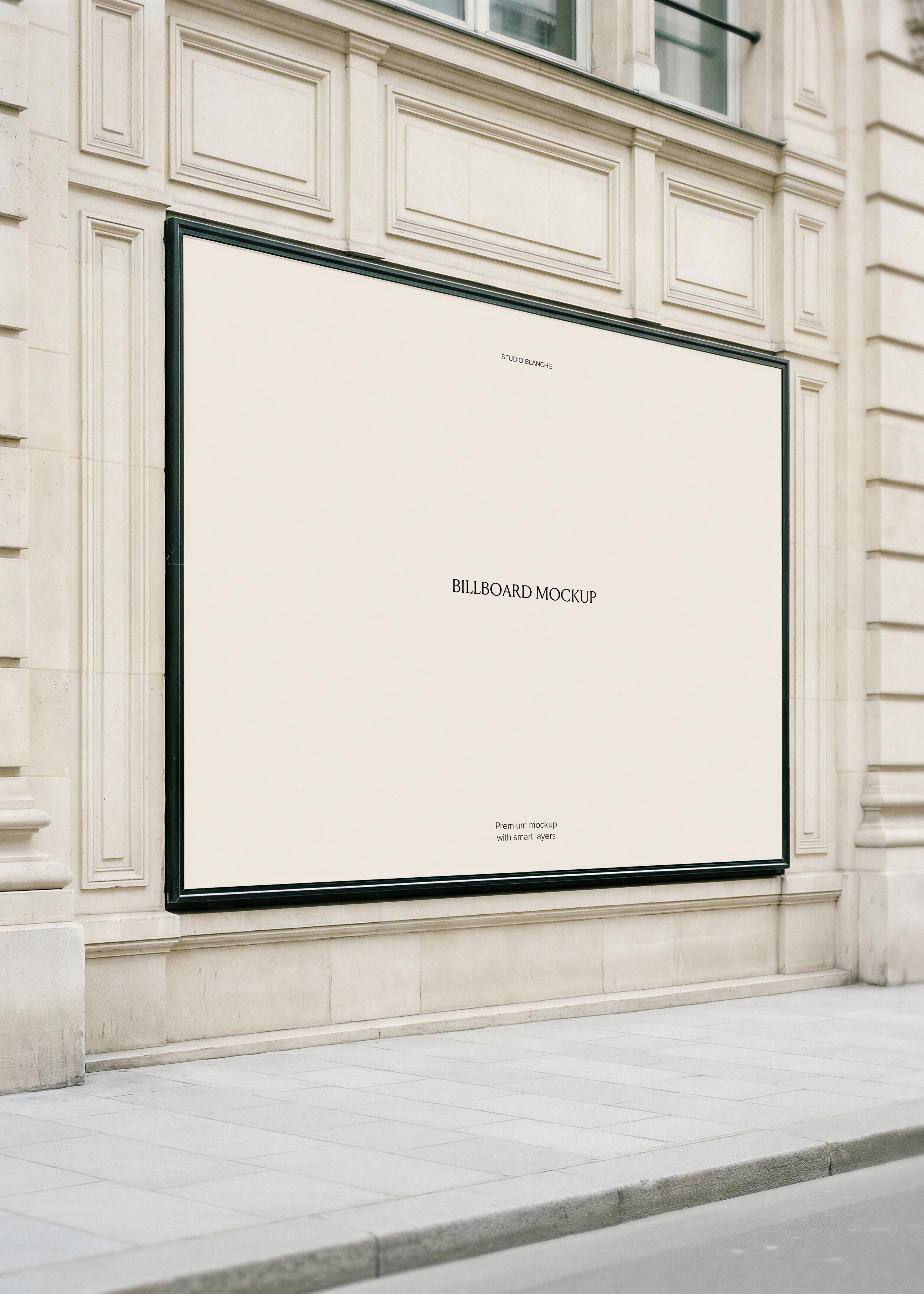 Blank cream billboard in a dark metal frame mounted on a grand Haussmann limestone building facade at street level, from Studio Blanche