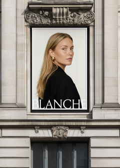 Black framed billboard mockup set into ornate stone facade above grand entrance, displaying fashion campaign artwork