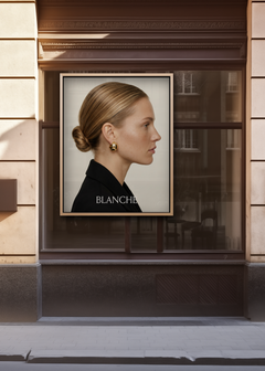 Gold framed window poster mockup in a dark European boutique shopfront, displaying editorial fashion campaign artwork