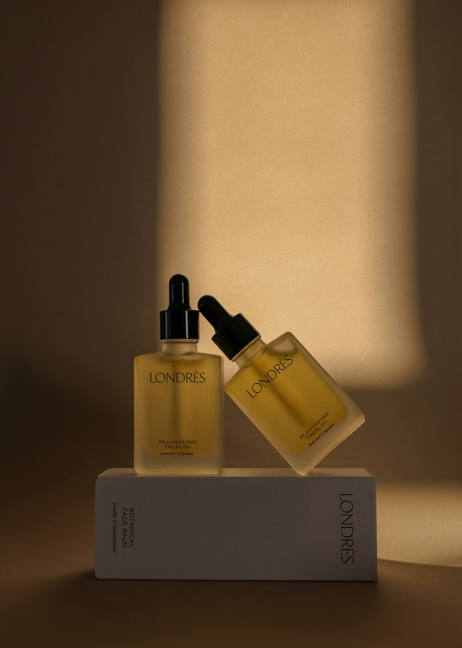 Two skincare bottles with droppers on a white stand against a warm brown background