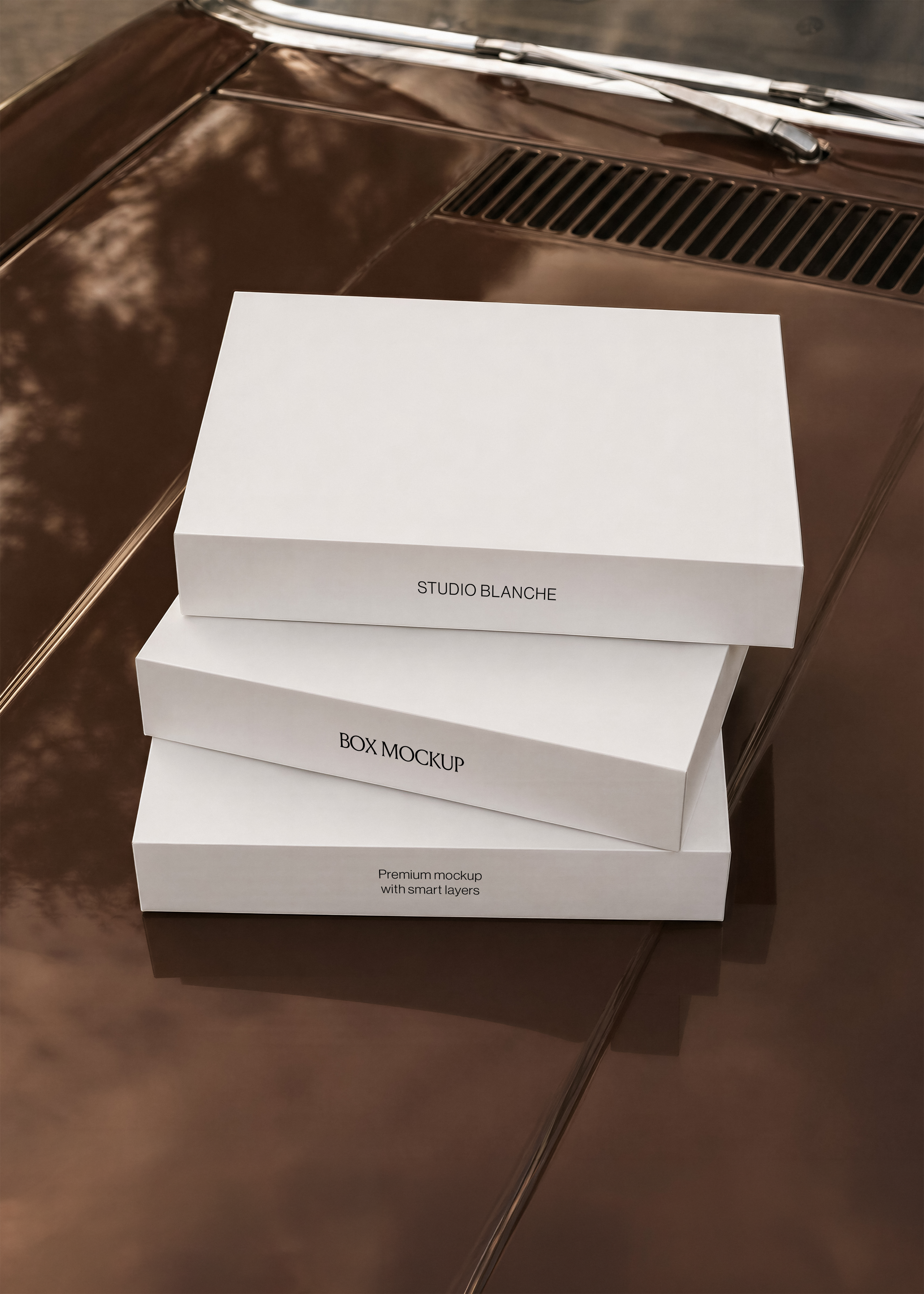 Gift box mockup, three white lidded boxes stacked at an angle on a glossy brown car bonnet beside a chrome wiper