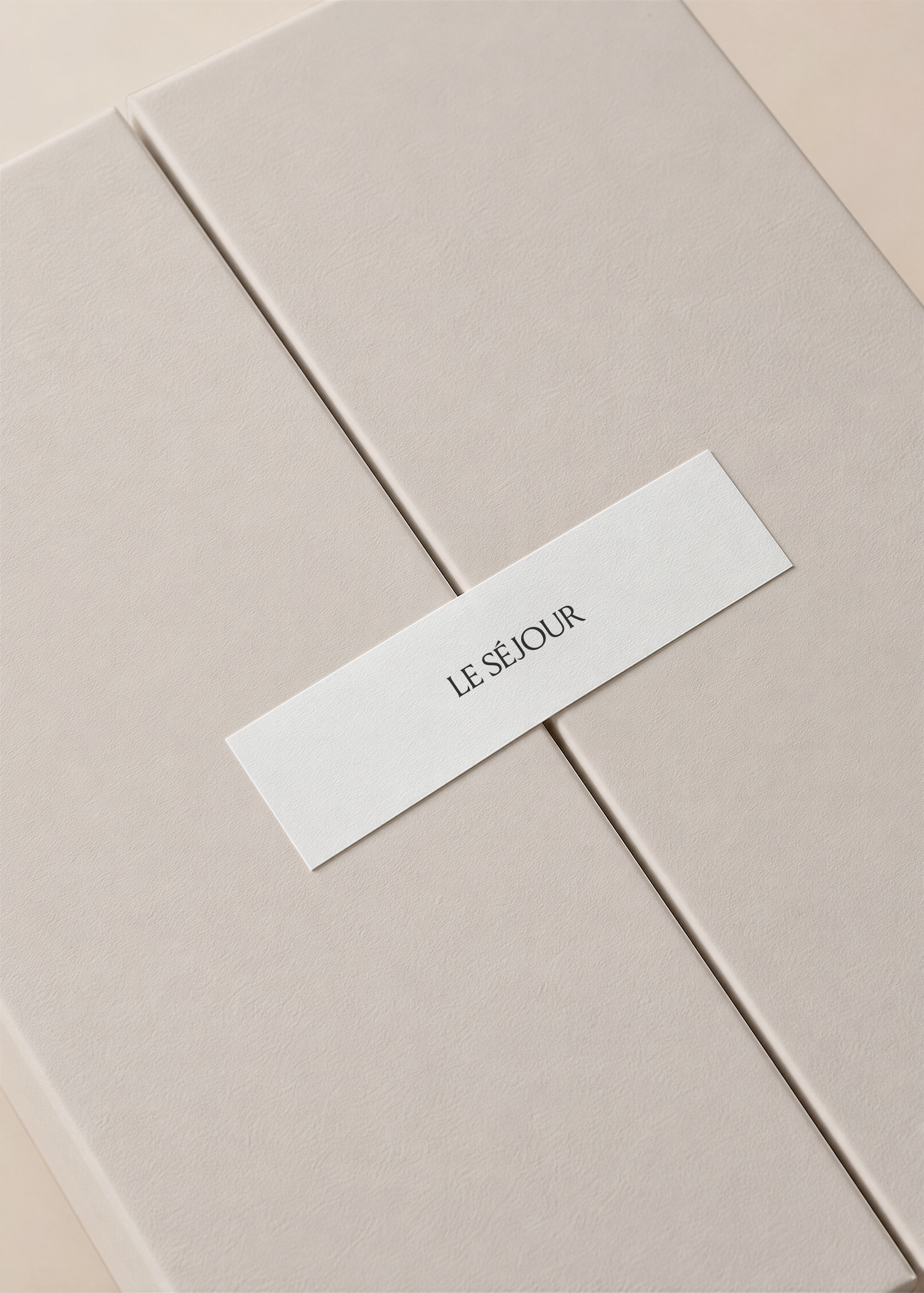 Gatefold gift box mockup in textured taupe card with a white paper label band across the opening, on a beige surface