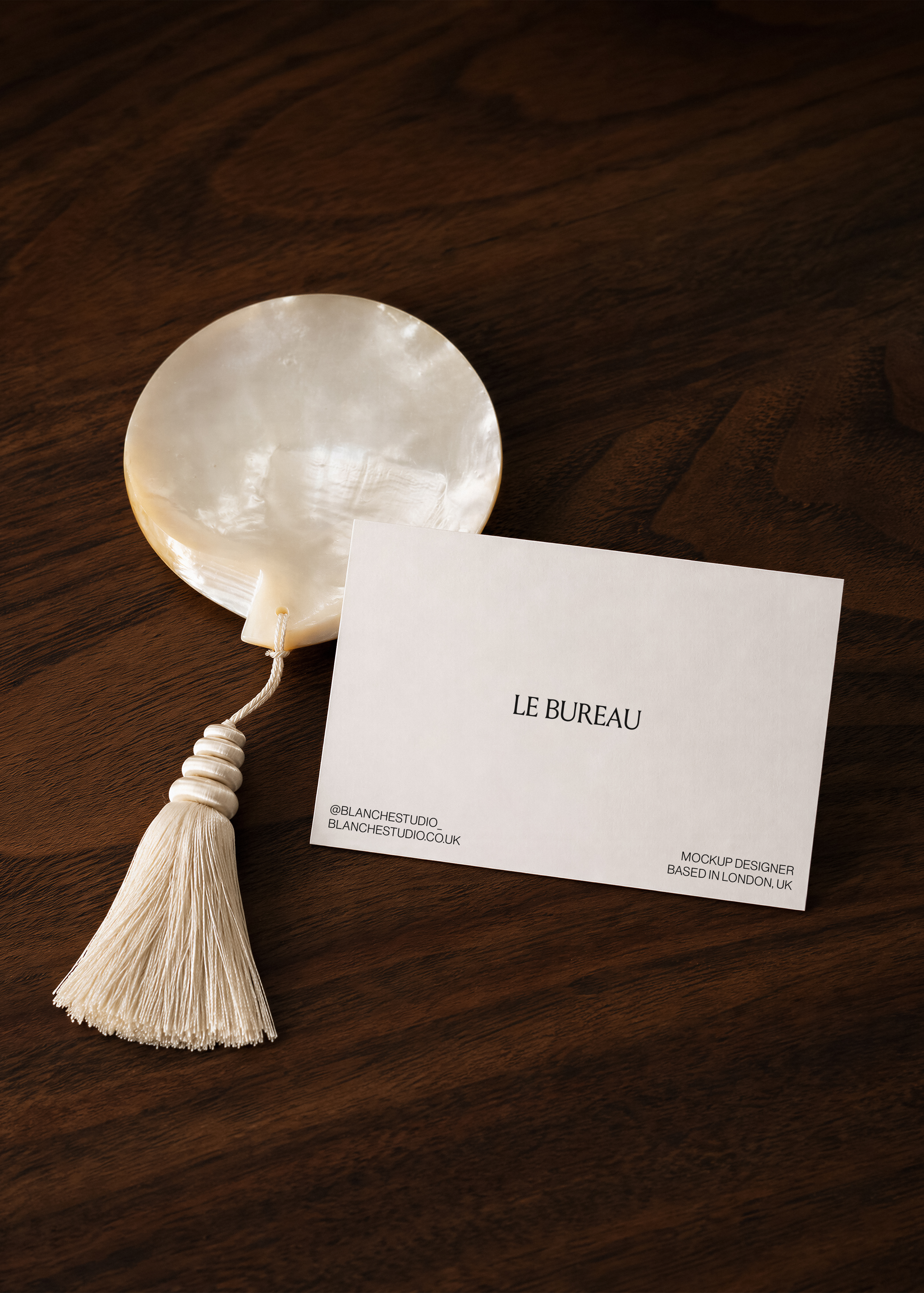 Business card mockup displaying Le Bureau branding on dark walnut surface, mother-of-pearl disc and cream tassel