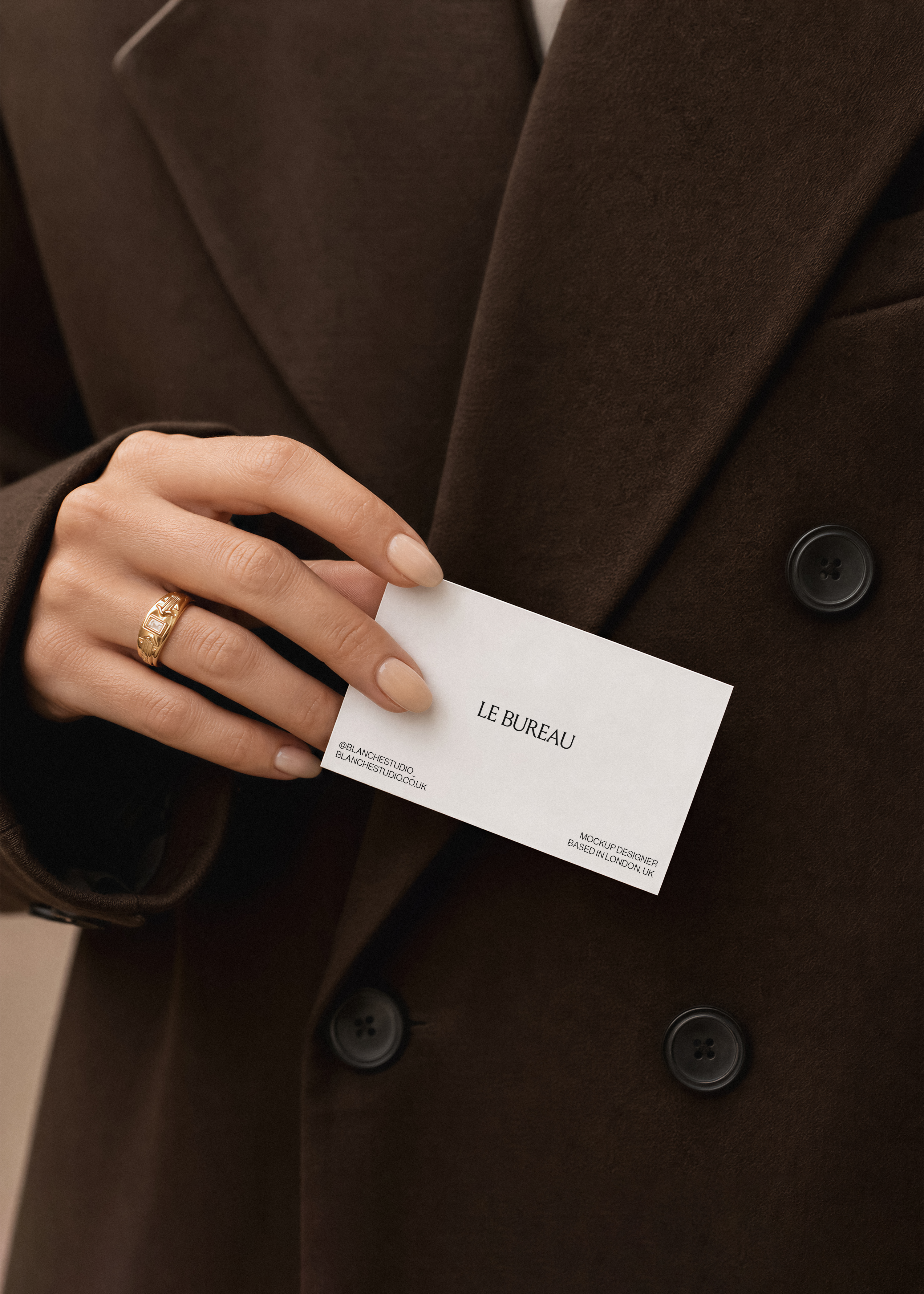 Business card mockup displaying Le Bureau branding held against dark wool coat, gold ring and neutral nail detail