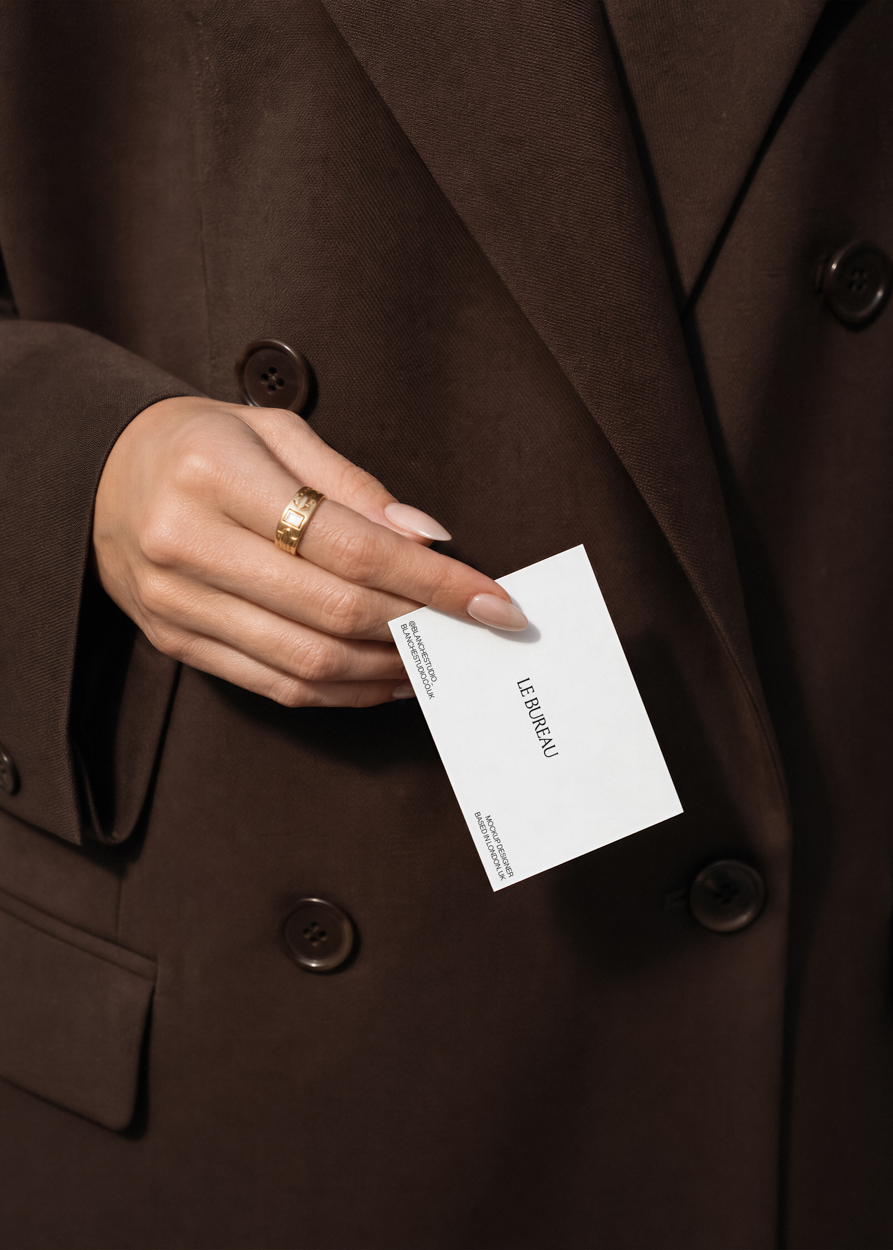 Business card mockup displaying Le Bureau branding in portrait, held from dark blazer pocket with gold band ring detail