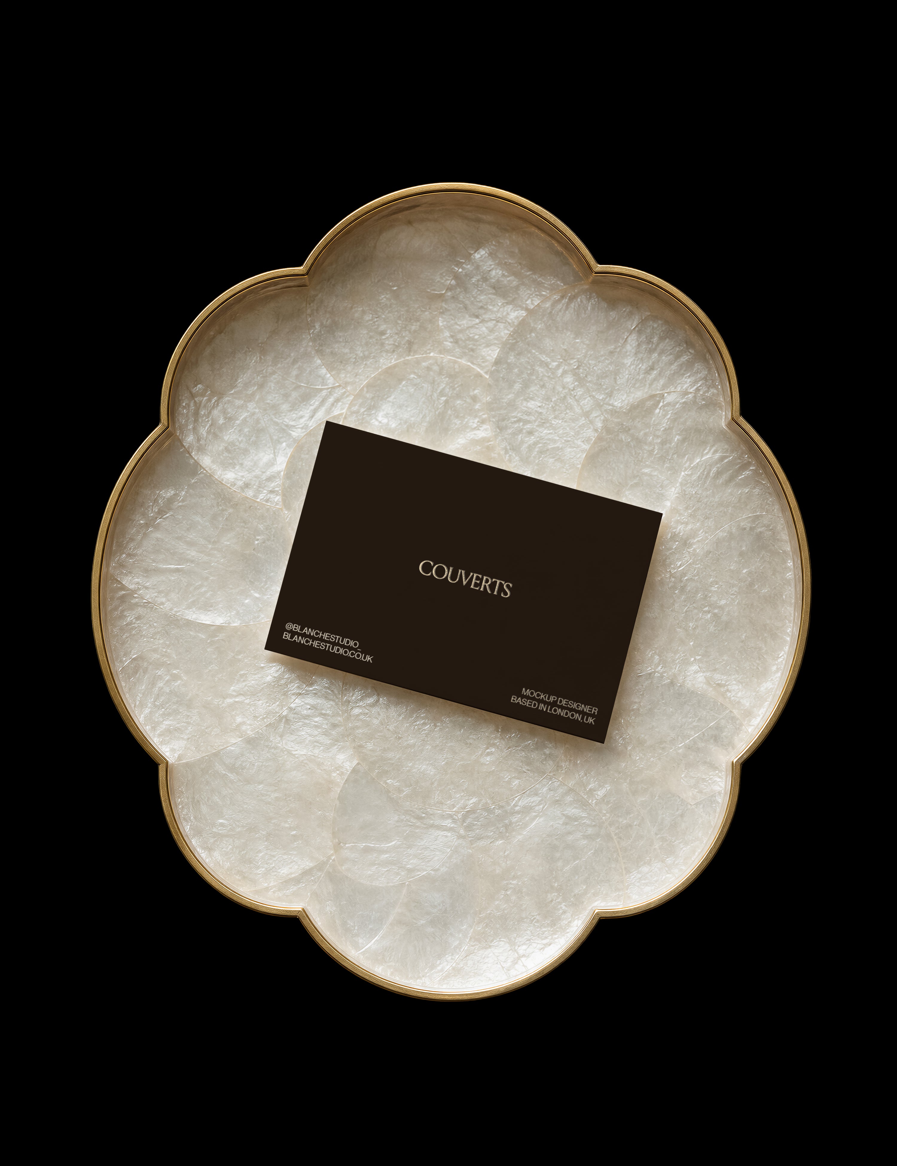 Dark business card mockup resting on a gold-rimmed flower-shaped tray lined with iridescent capiz shell on black