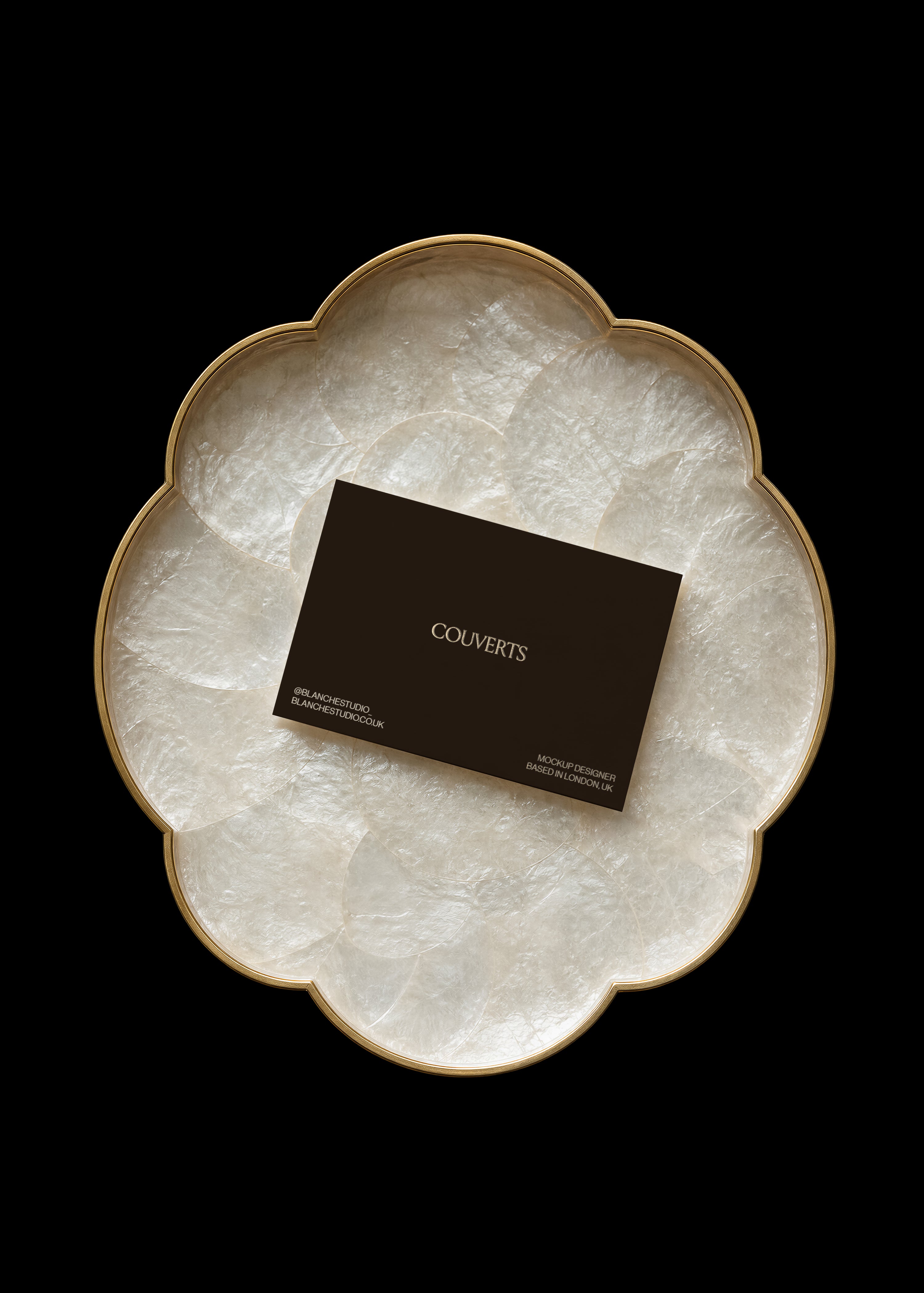 Dark business card mockup resting on a gold-rimmed flower-shaped tray lined with iridescent capiz shell on black