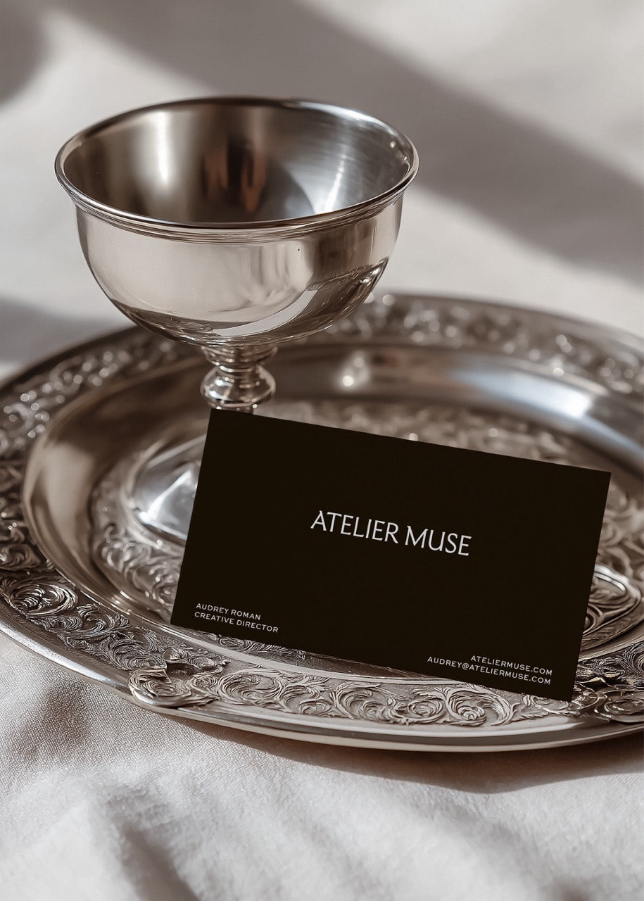Silver goblet and ornate tray with 'Atelier Muse' business card on a light background