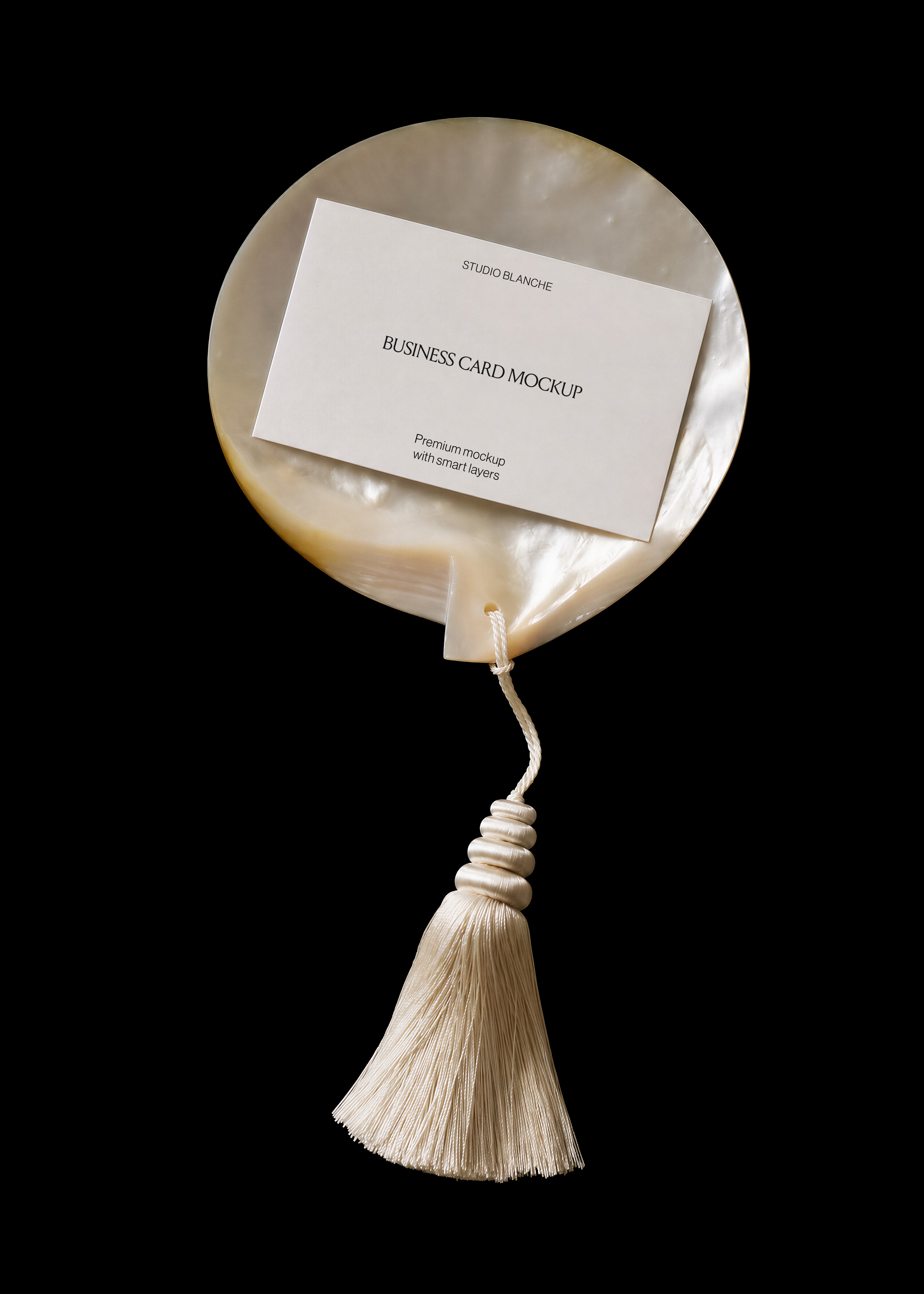 White business card mockup on iridescent pearl shell, centred text layout, cream tassel below, dark editorial scene