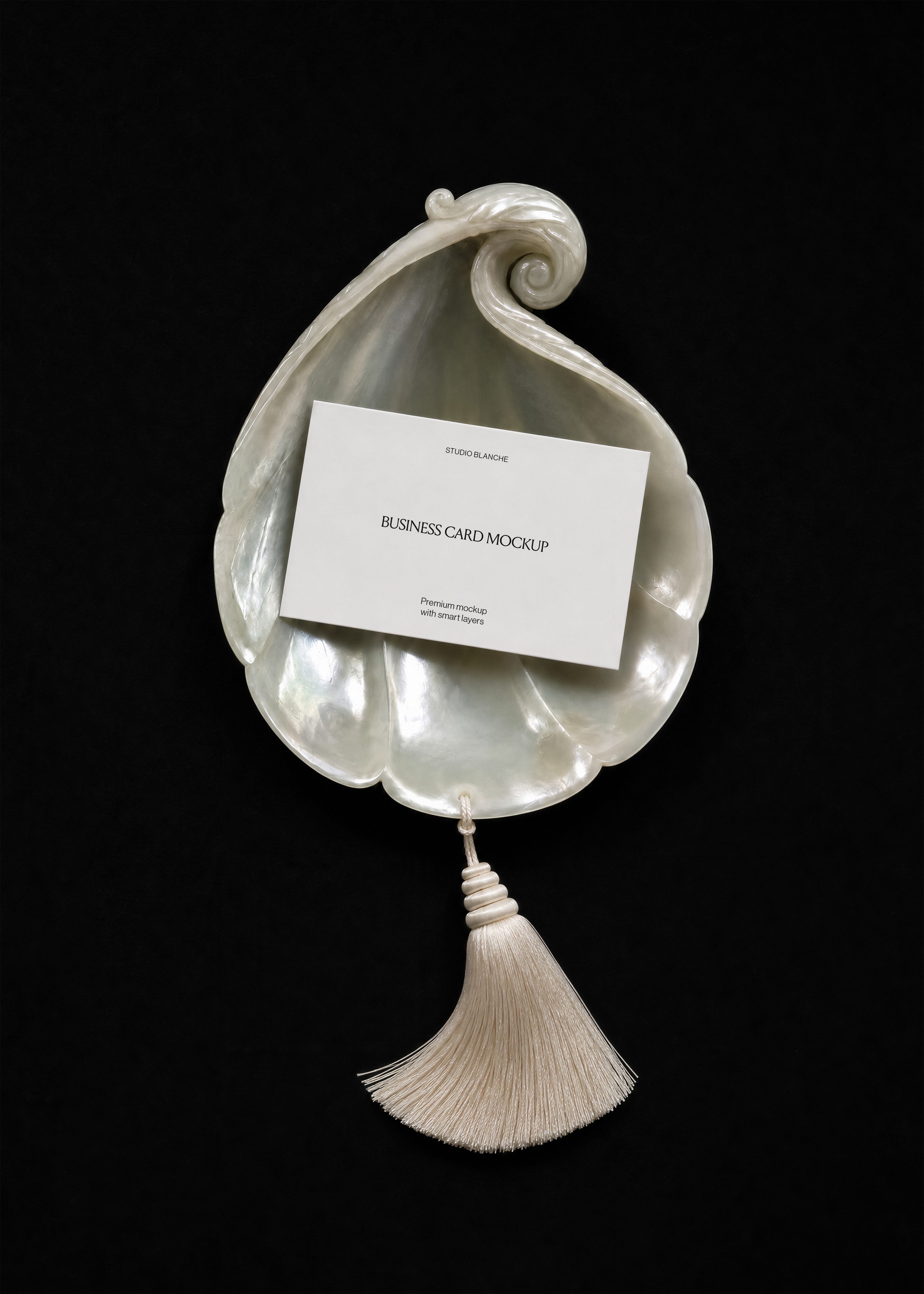 White business card mockup on iridescent pearl shell, centred text layout, cream tassel below, dark editorial scene