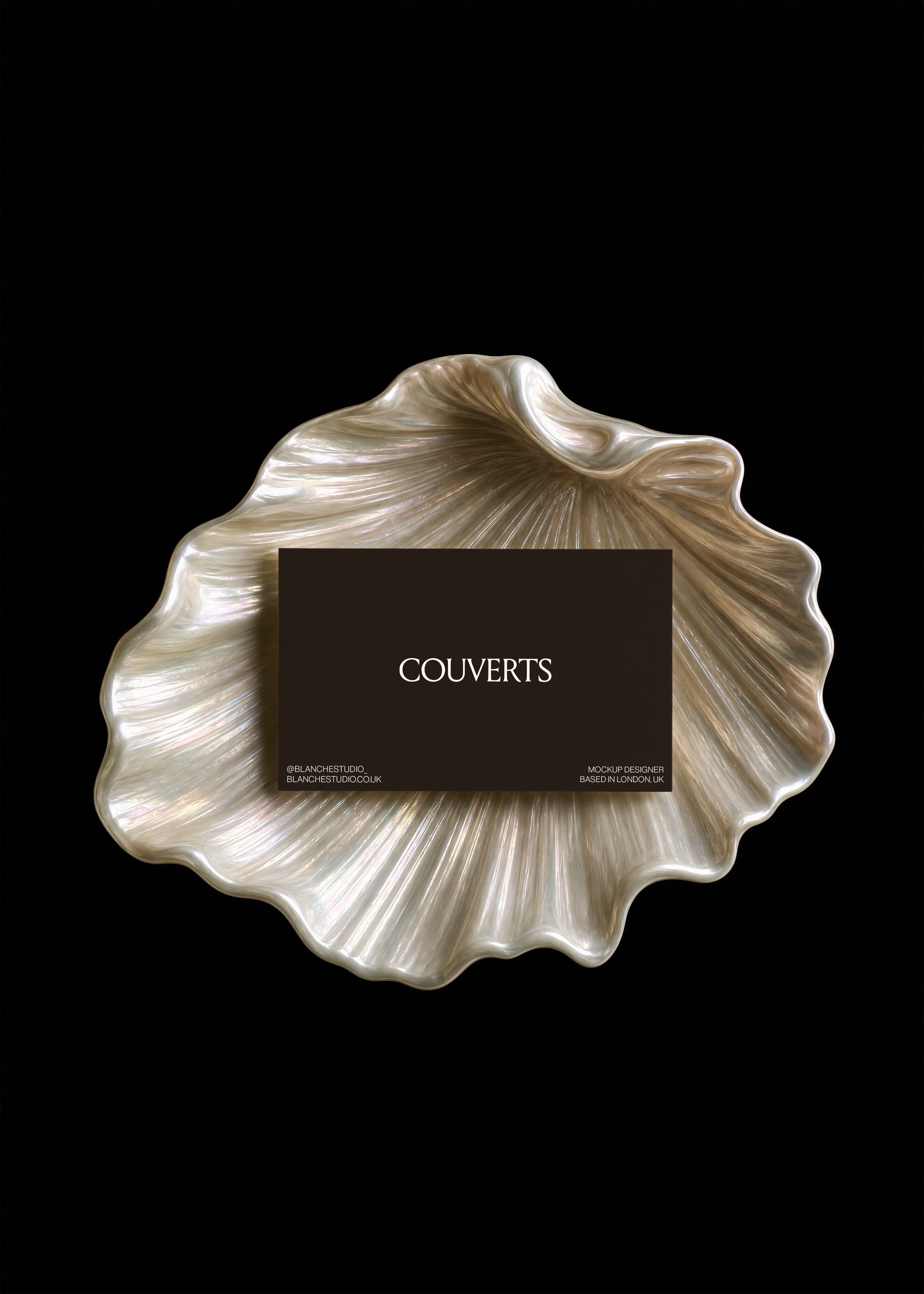 Dark brown business card with serif logo resting on an iridescent mother of pearl shell dish against a black background