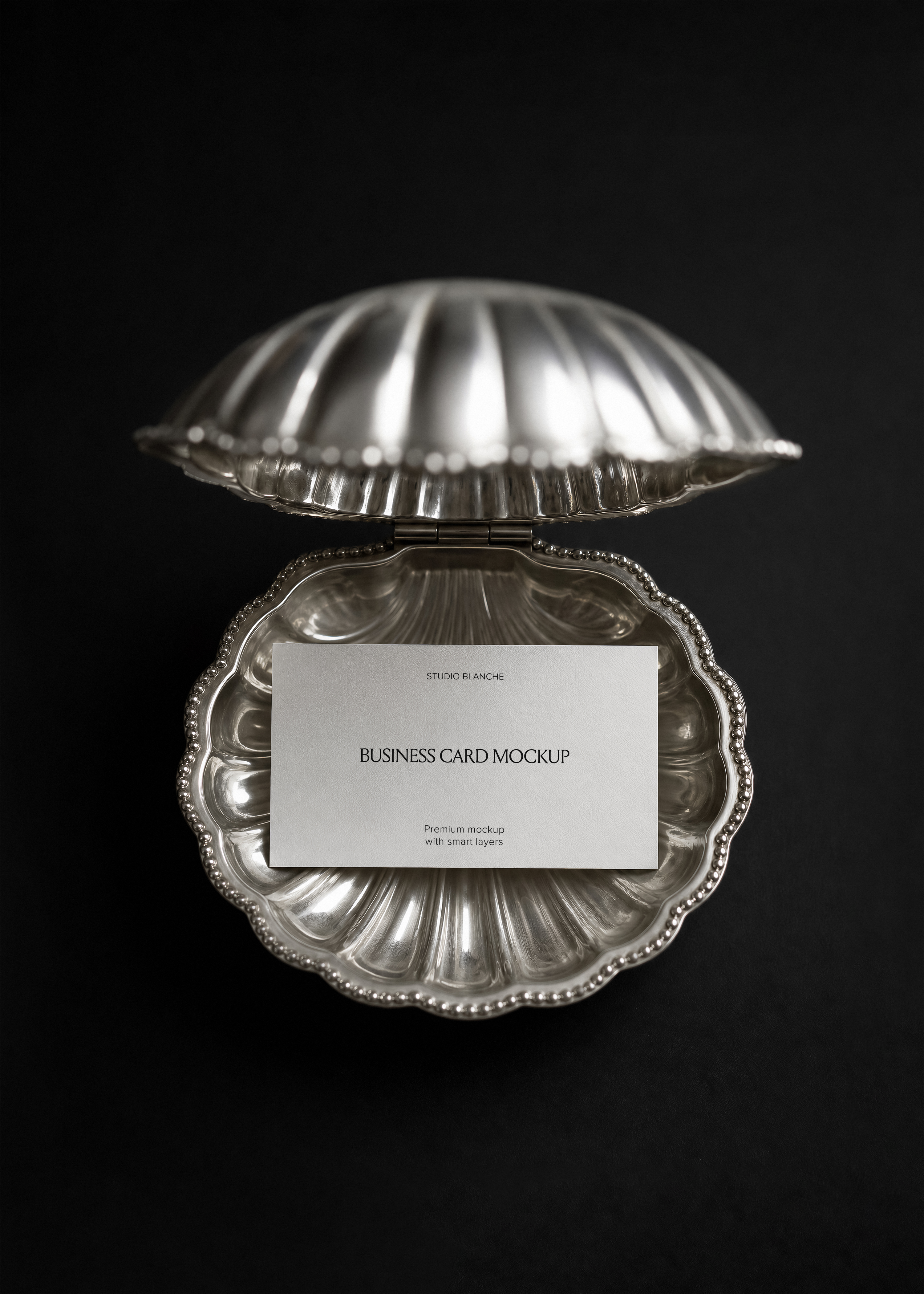 Cream business card with serif logo and script subheading set inside a silver shell dish, black backdrop, top down view