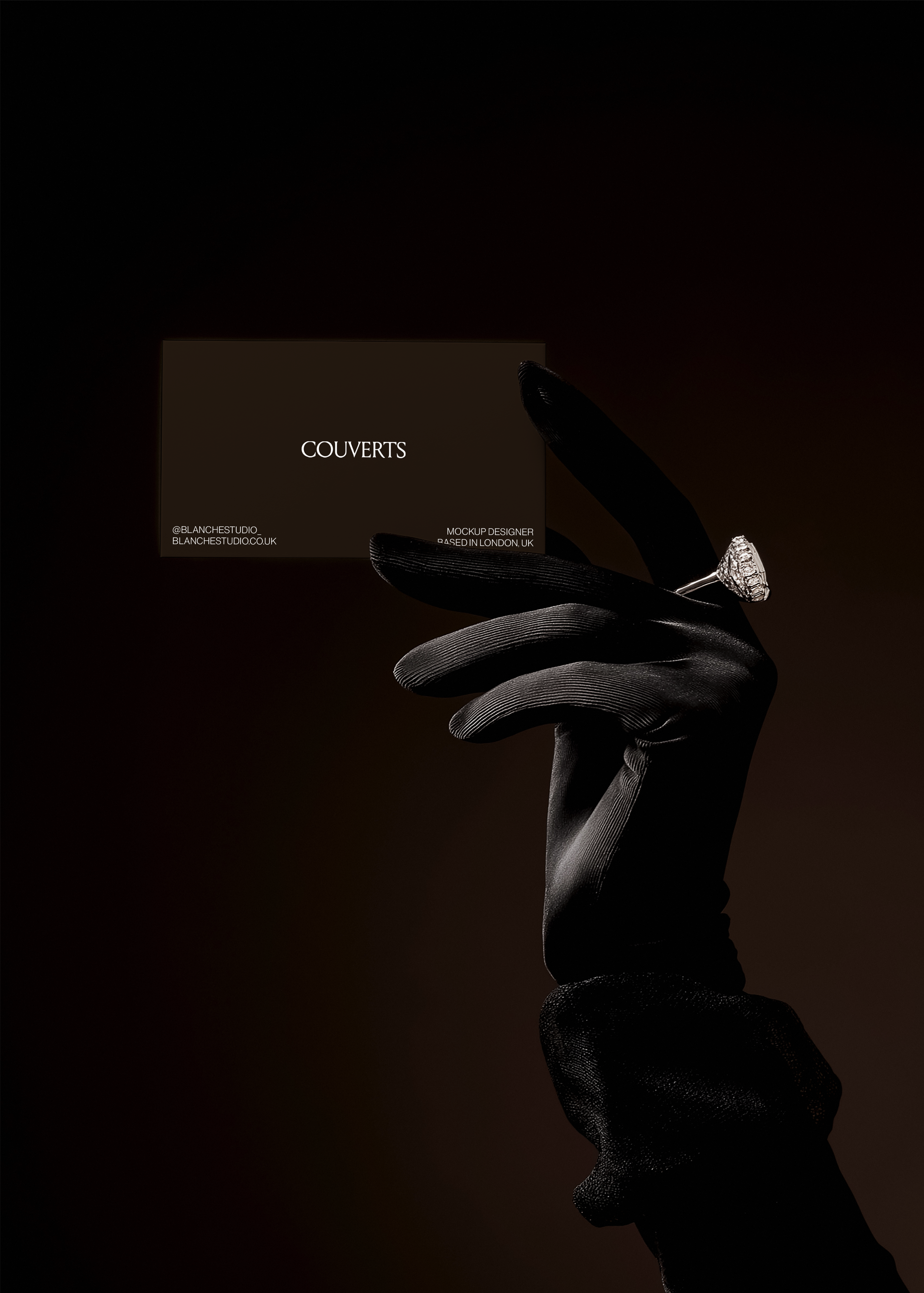 Business card mockup held between gloved fingers with diamond ring, dark brown background, dramatic low-light styling