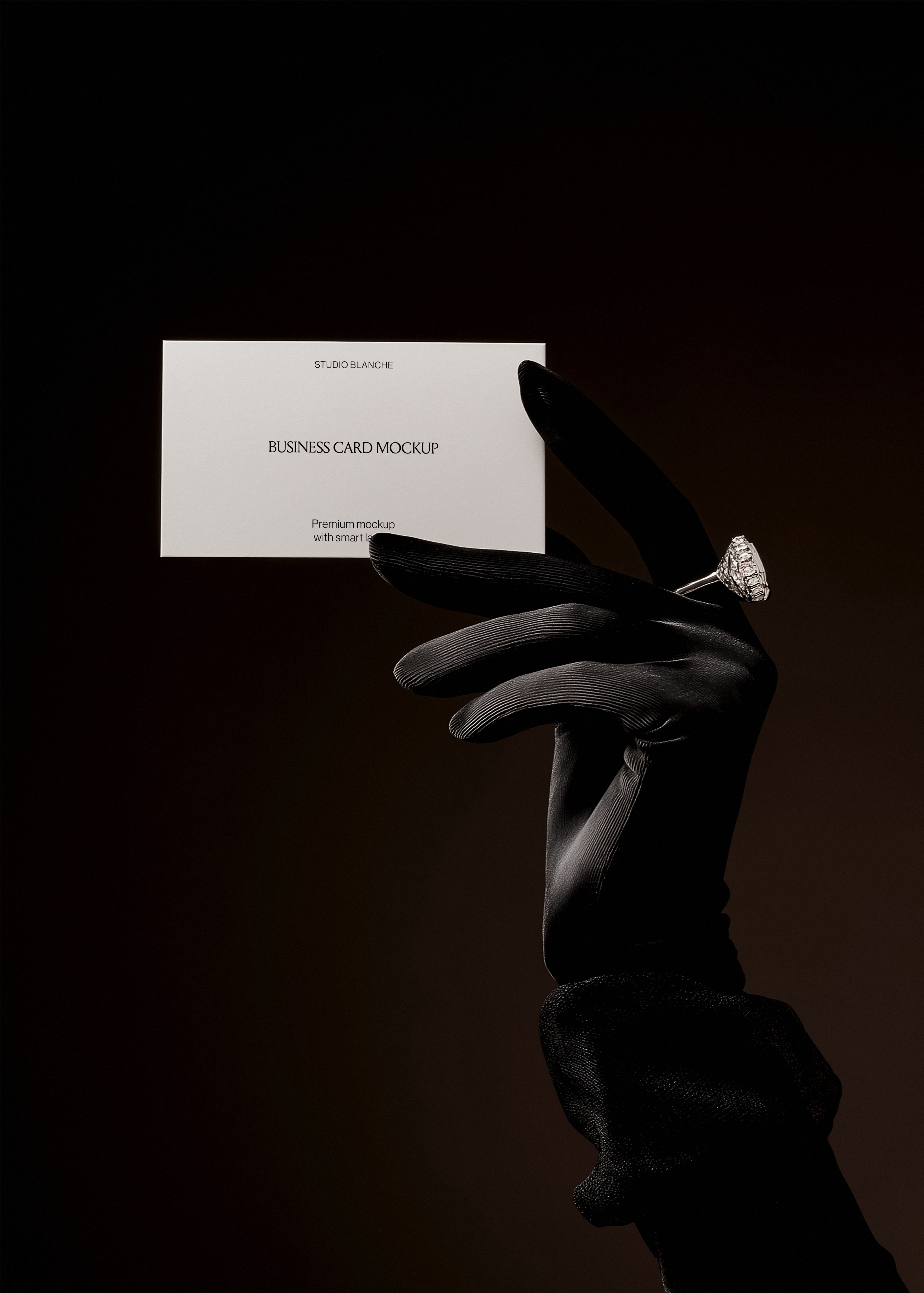 Close-up of cream business card with serif logo, glove and diamond ring visible at edge, moody dark backdrop