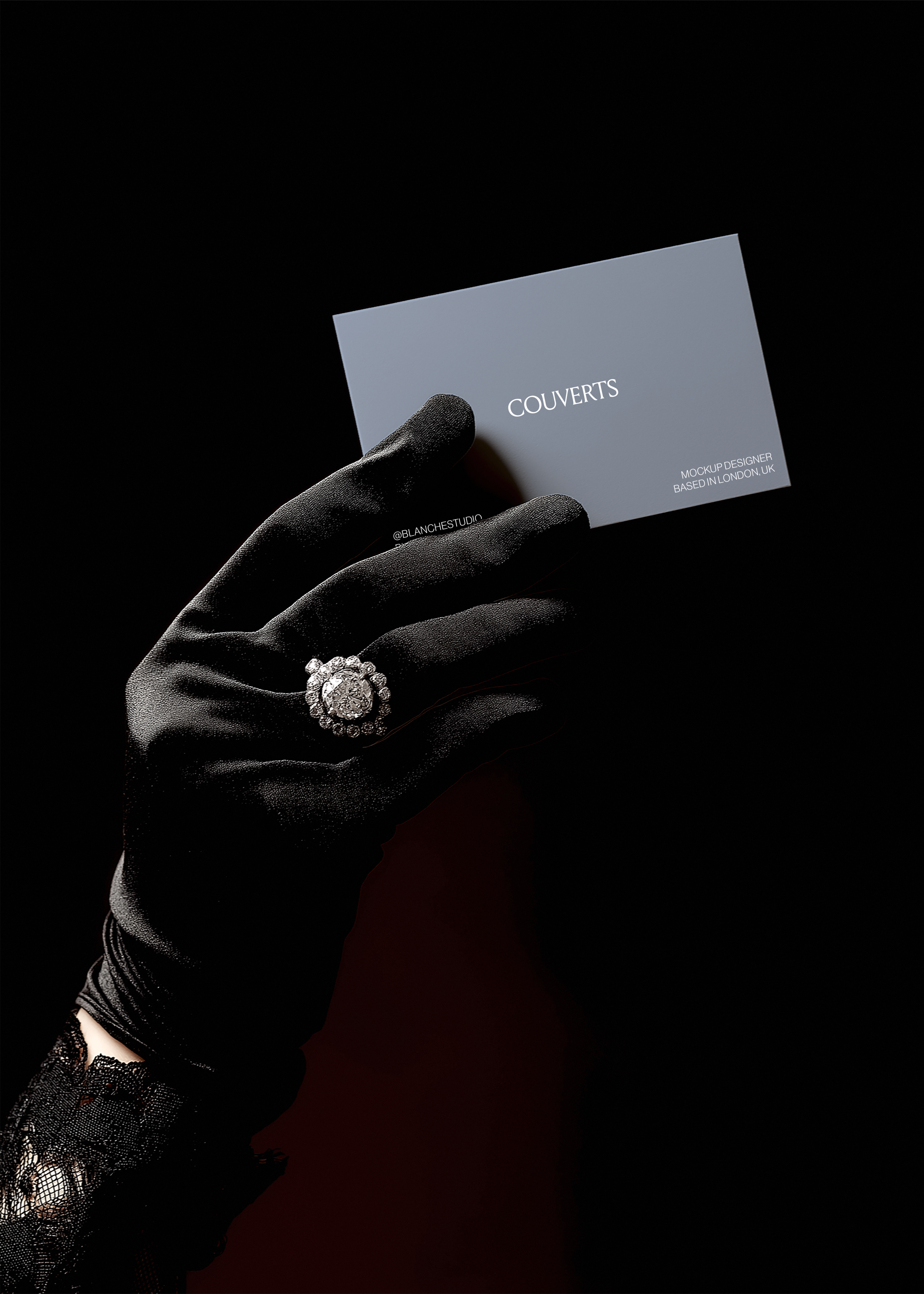 Business card mockup held by gloved hand wearing diamond cluster ring, lace cuff visible, black background, vintage noir styling