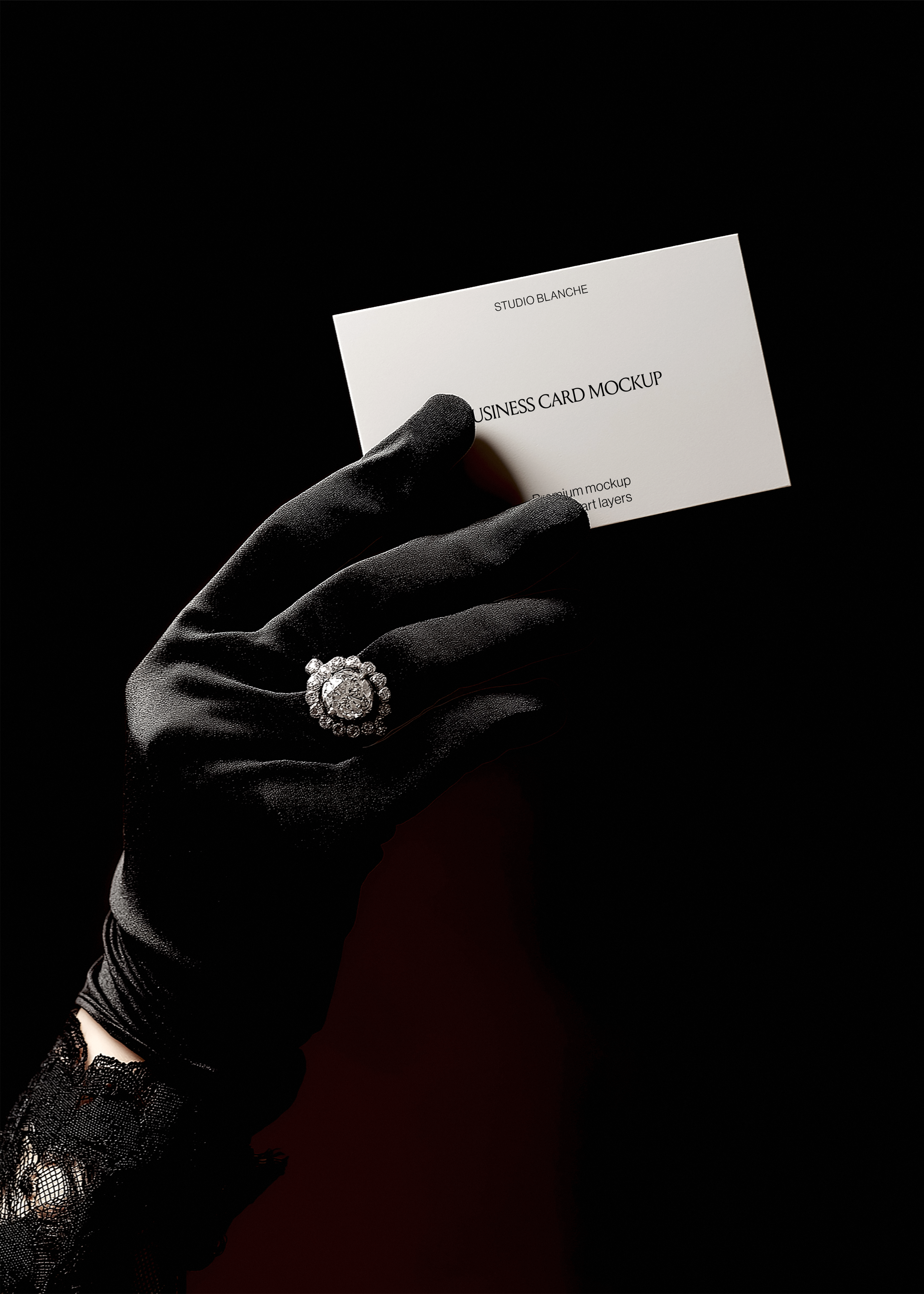 Close-up of pale grey business card with serif logo, satin glove and vintage diamond ring at edge, dark moody backdrop