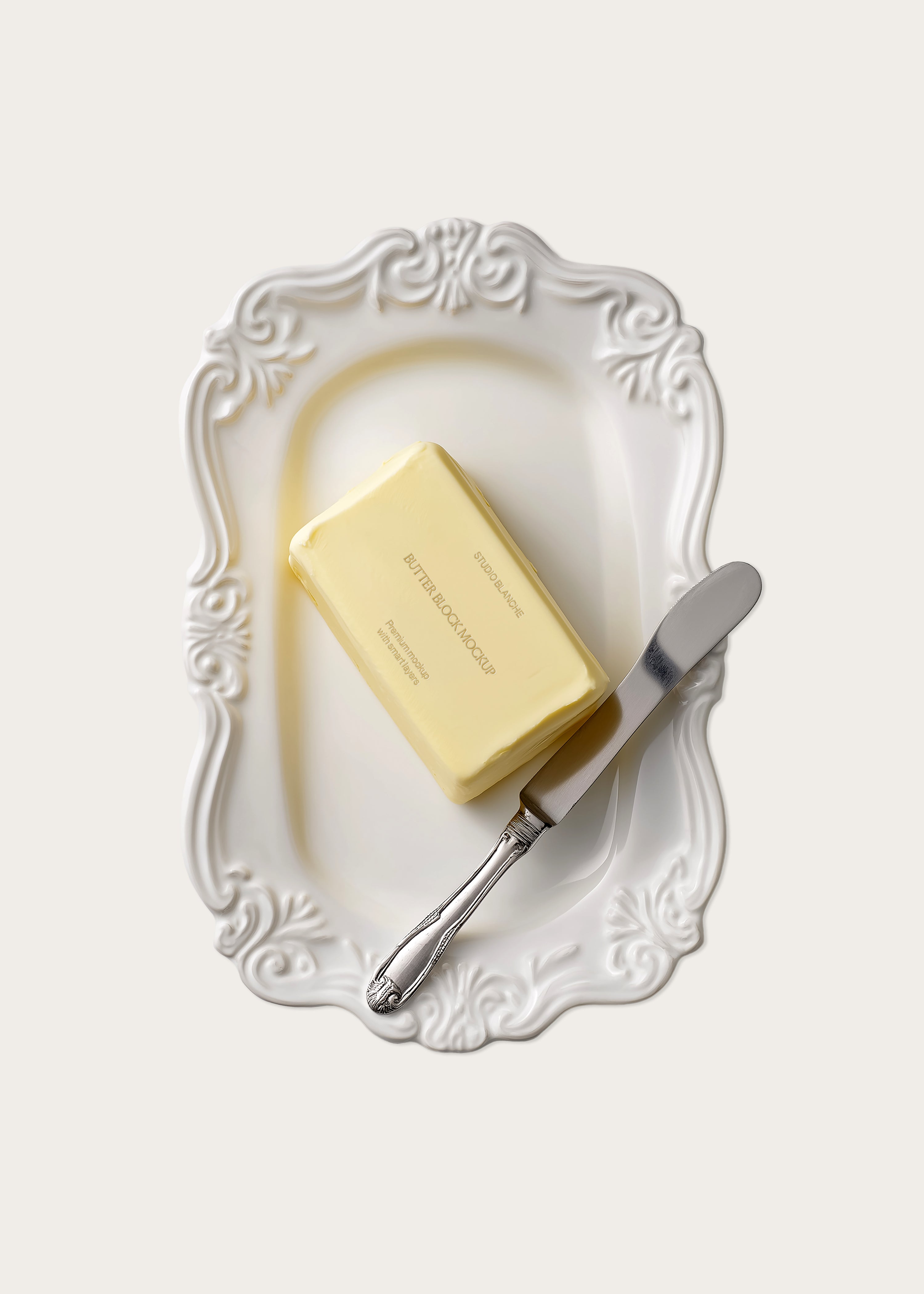 Butter block packaging mockup on decorative white baroque ceramic plate with antique silver knife, overhead view, cream background