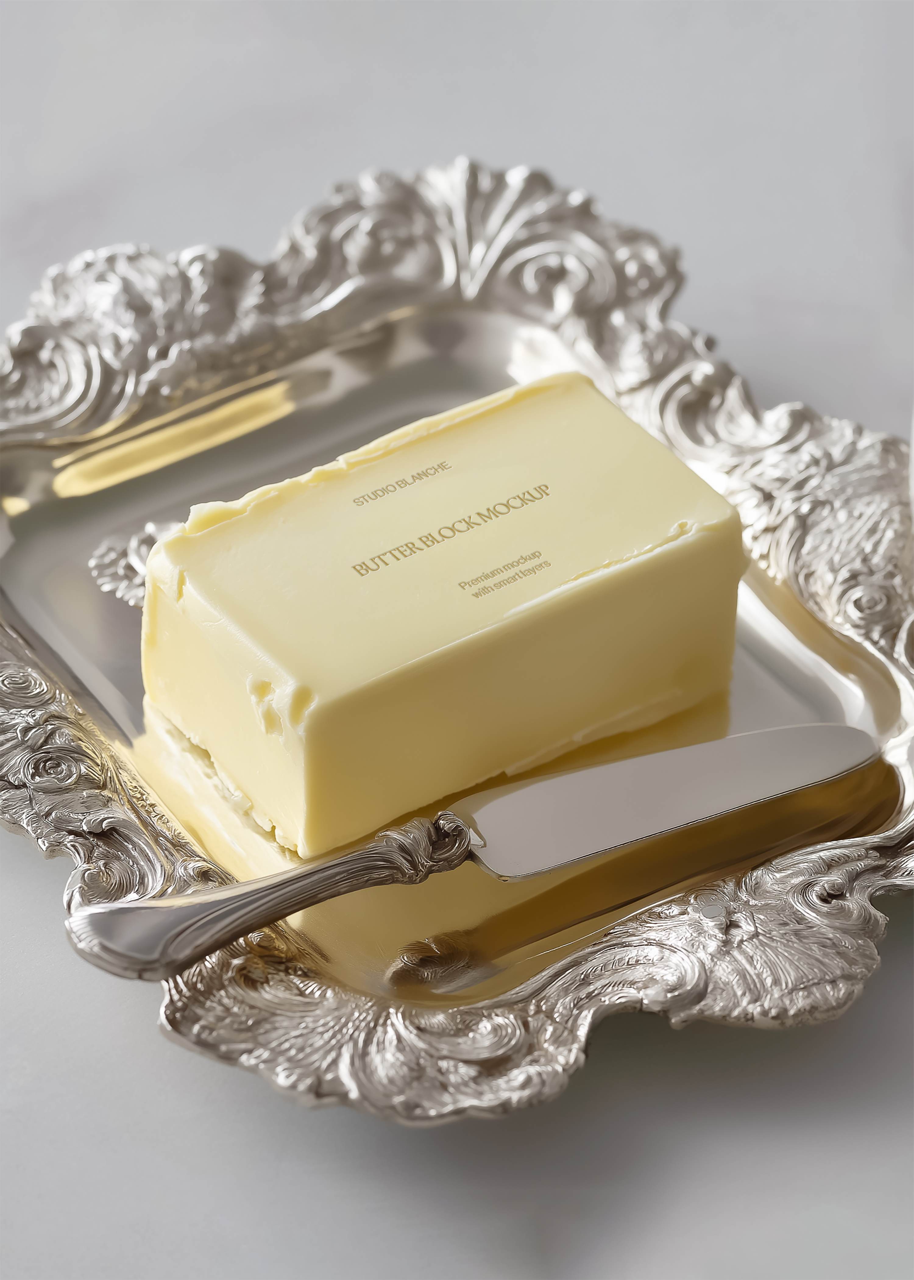 Butter block mockup on decorative silver tray with ornate butter knife, close front angle, soft daylight, grey background