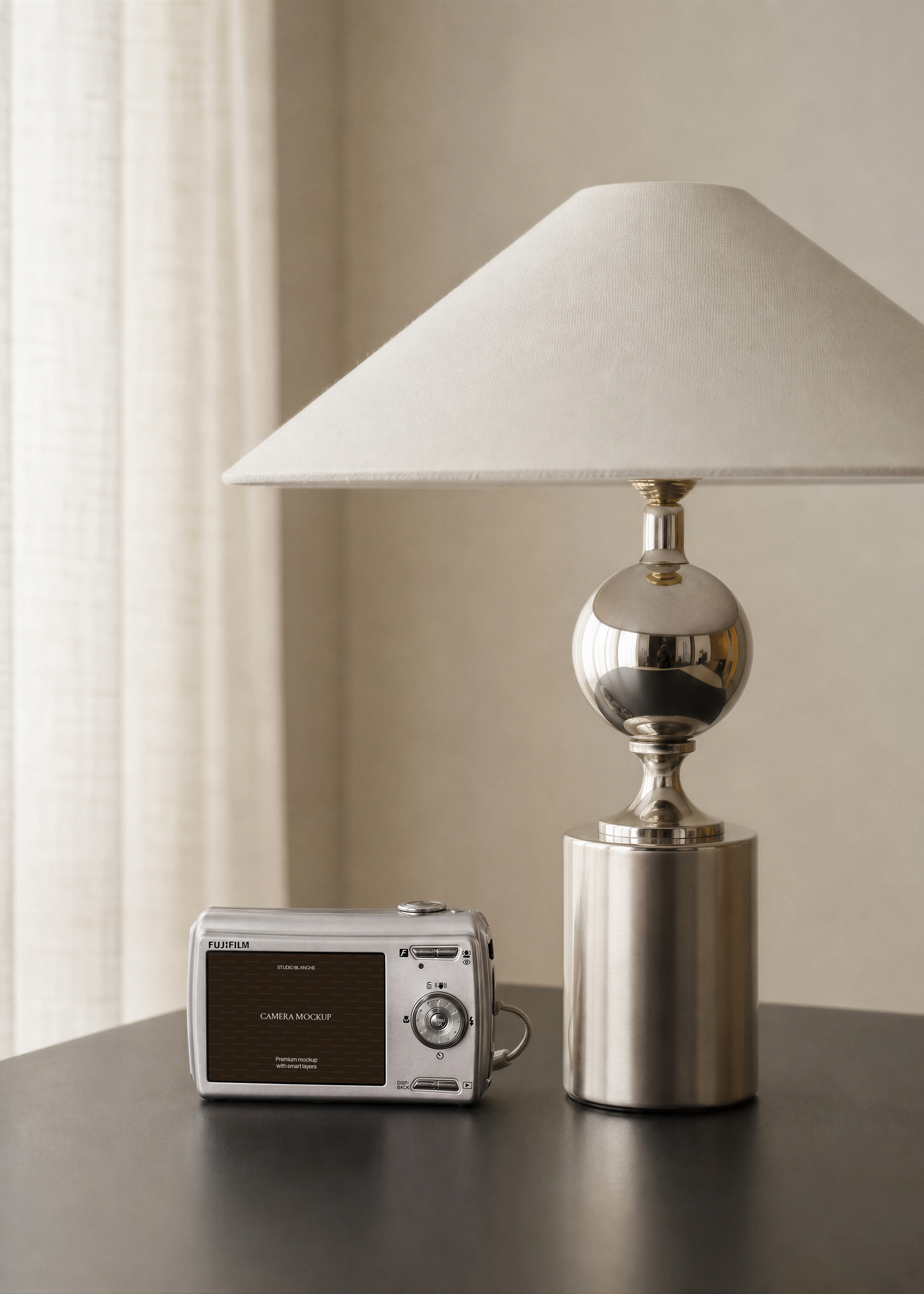 Compact digital camera mockup with brown screen graphic beside cream linen lampshade and polished chrome lamp base