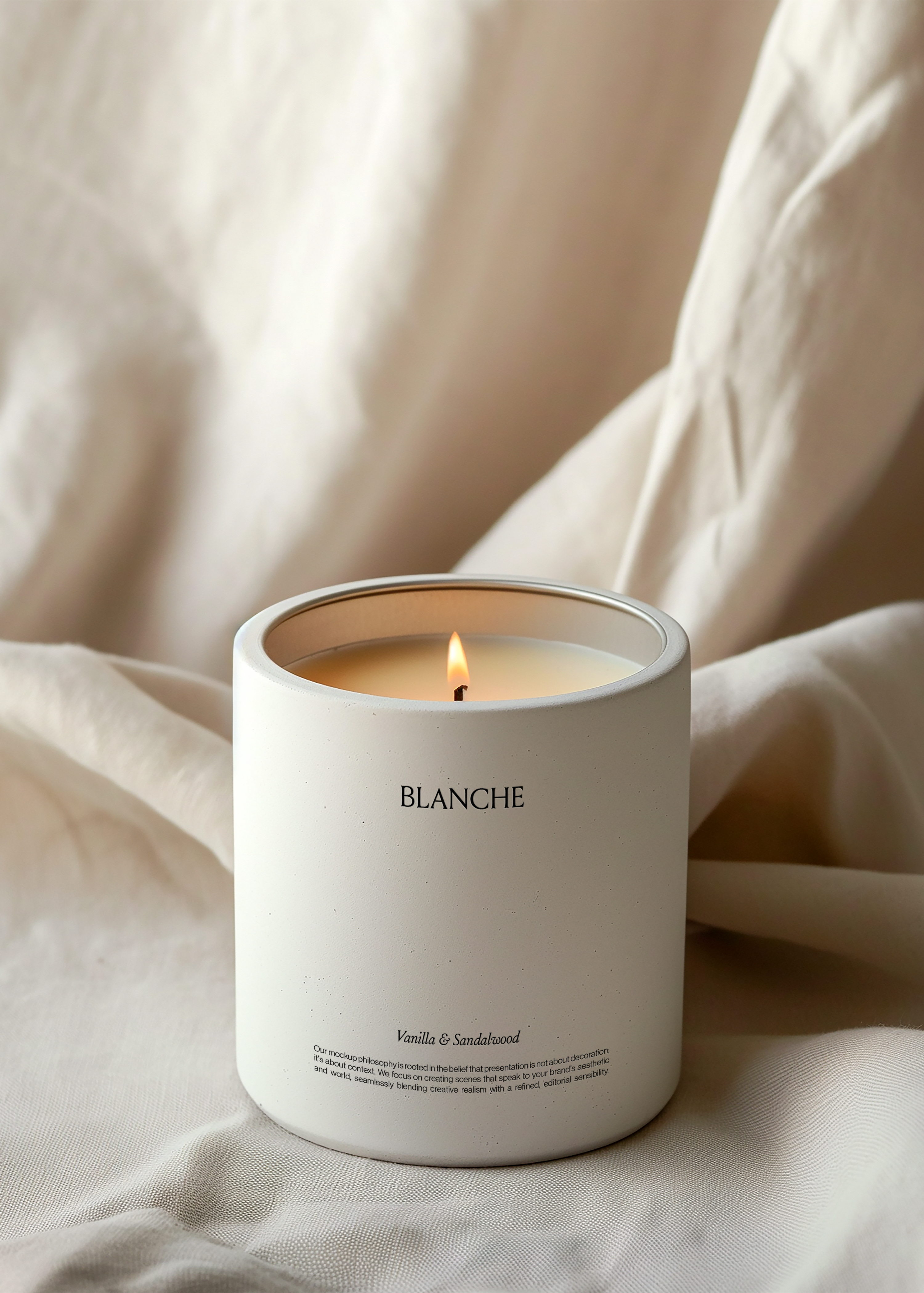 White concrete candle vessel with lit flame, styled on draped cream linen fabric, warm minimal scene