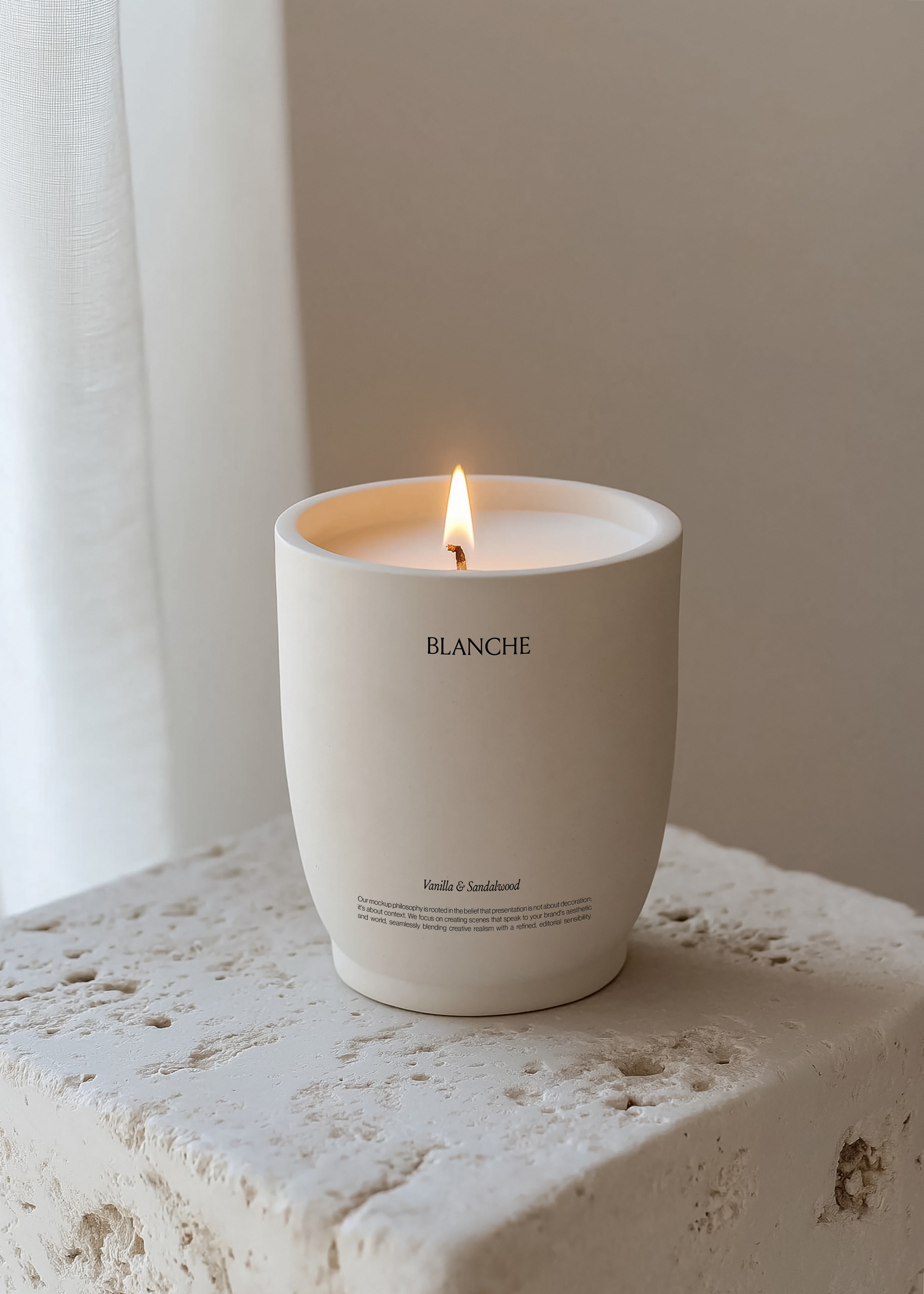 White ceramic tapered candle vessel with lit flame on rough travertine ledge, sheer curtain and neutral wall behind