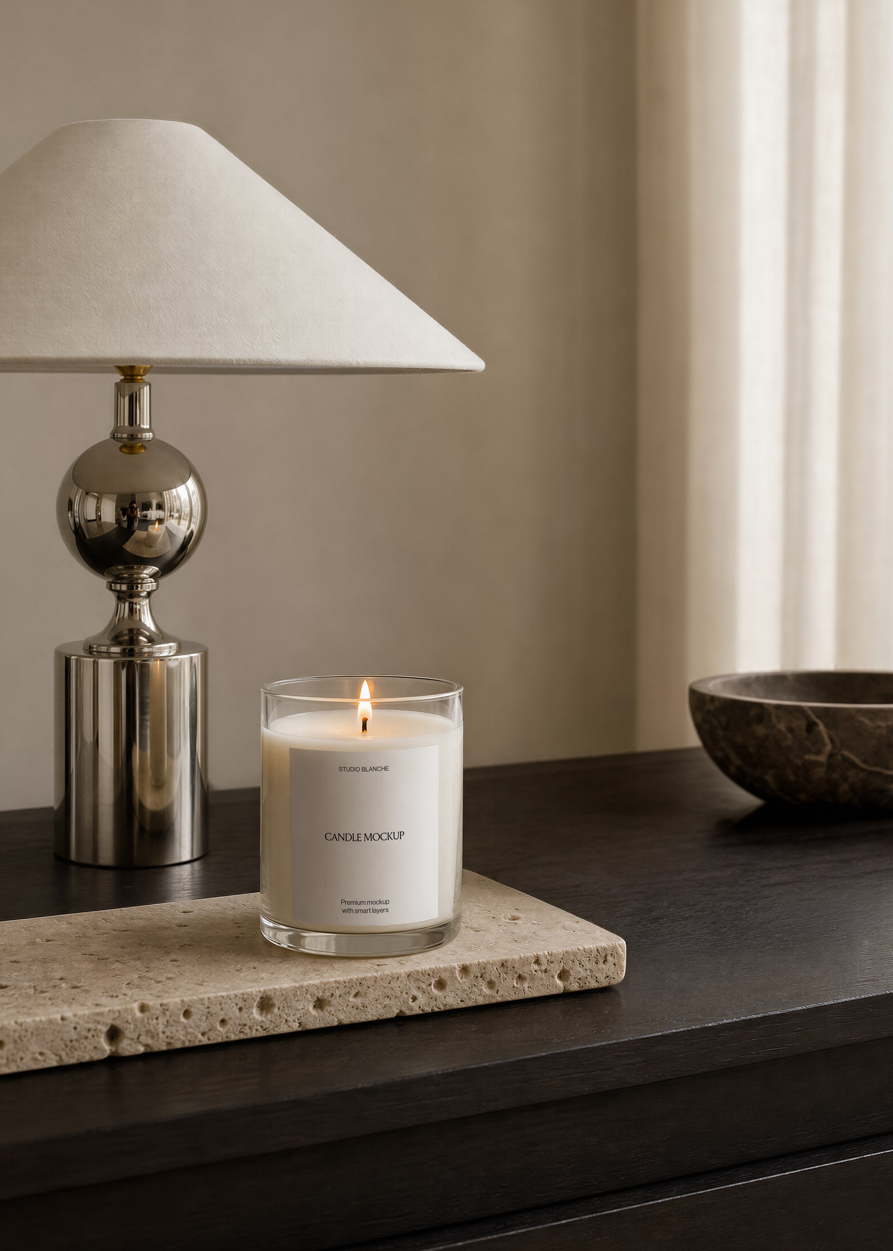 Glass candle jar mockup with plain white label, standing on textured travertine stone near a marble bowl