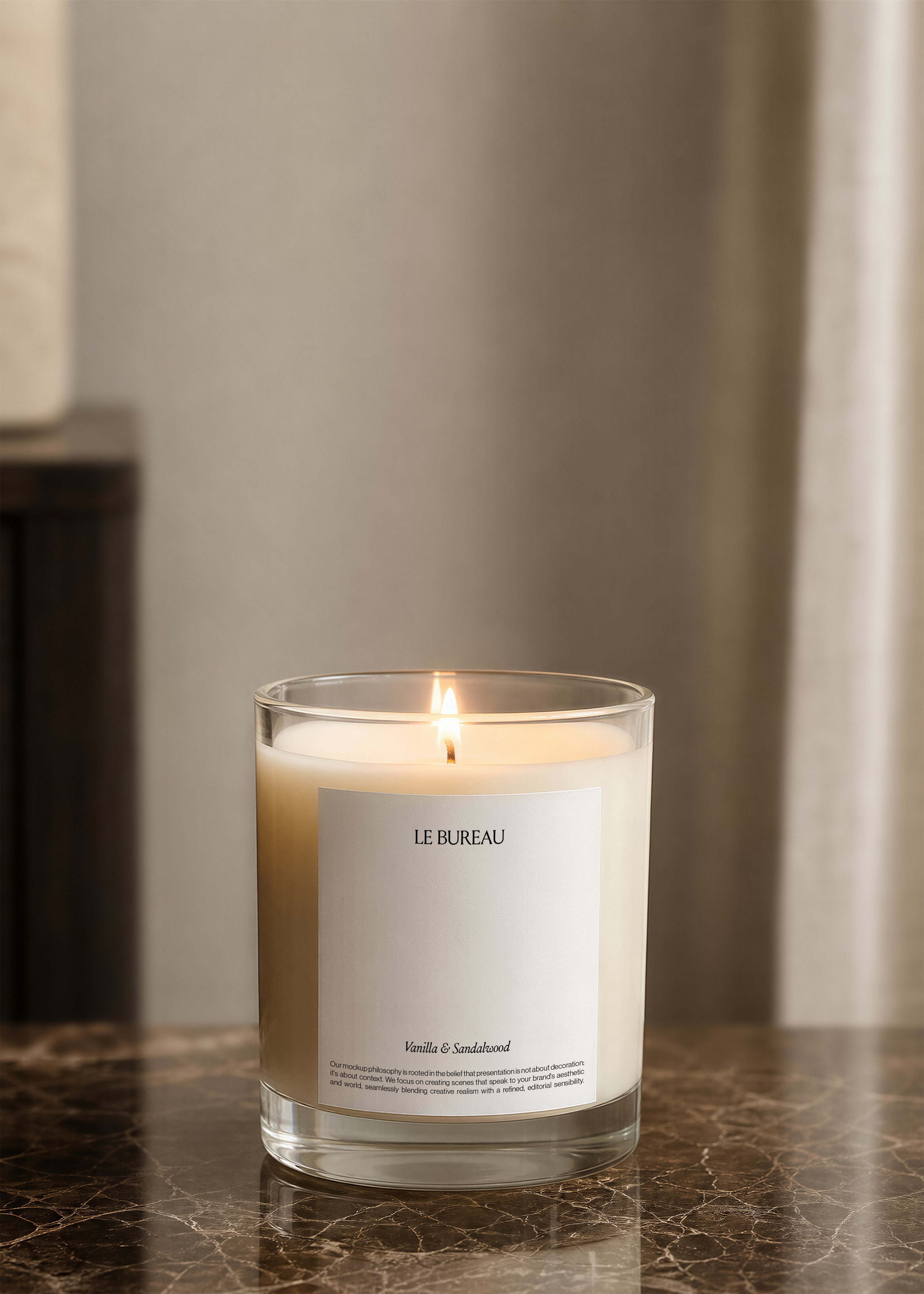 Lit glass candle jar mockup with pale label centred on dark marble, soft blurred warm interior background