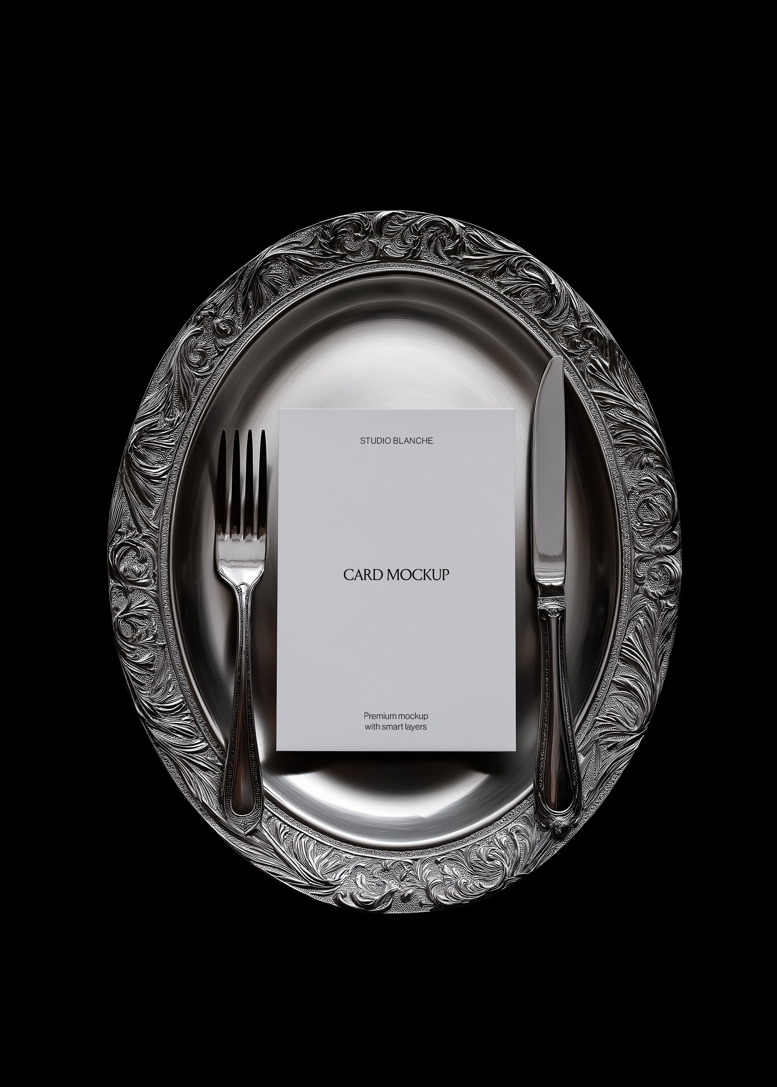 Card mockup detail showing engraved scrollwork rim on silver charger, polished cutlery, white card with black text