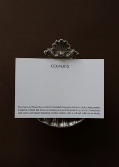 Landscape card mockup held by ornate silver shell clip against deep brown backdrop, close cropped vintage styling