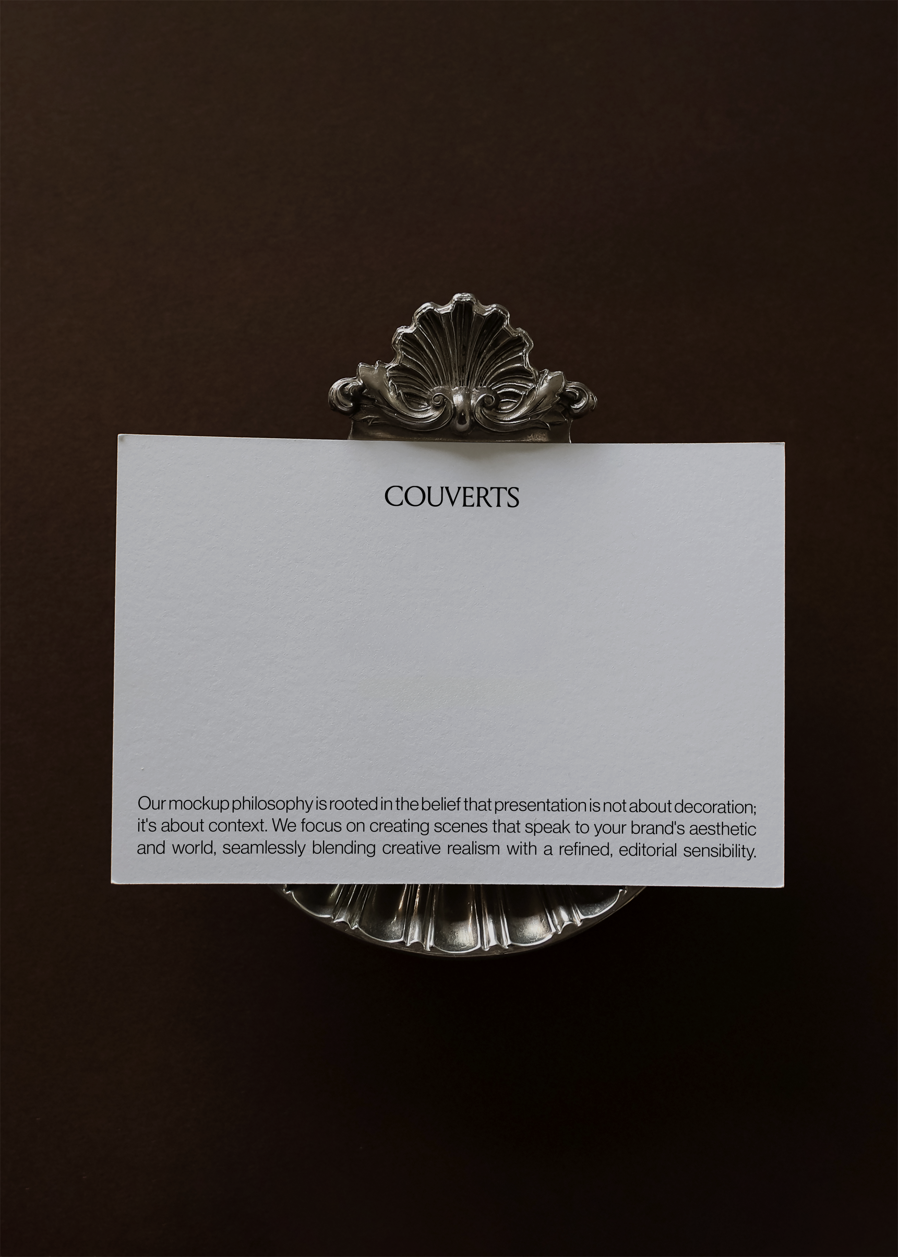 Landscape card mockup held by ornate silver shell clip against deep brown backdrop, close cropped vintage styling