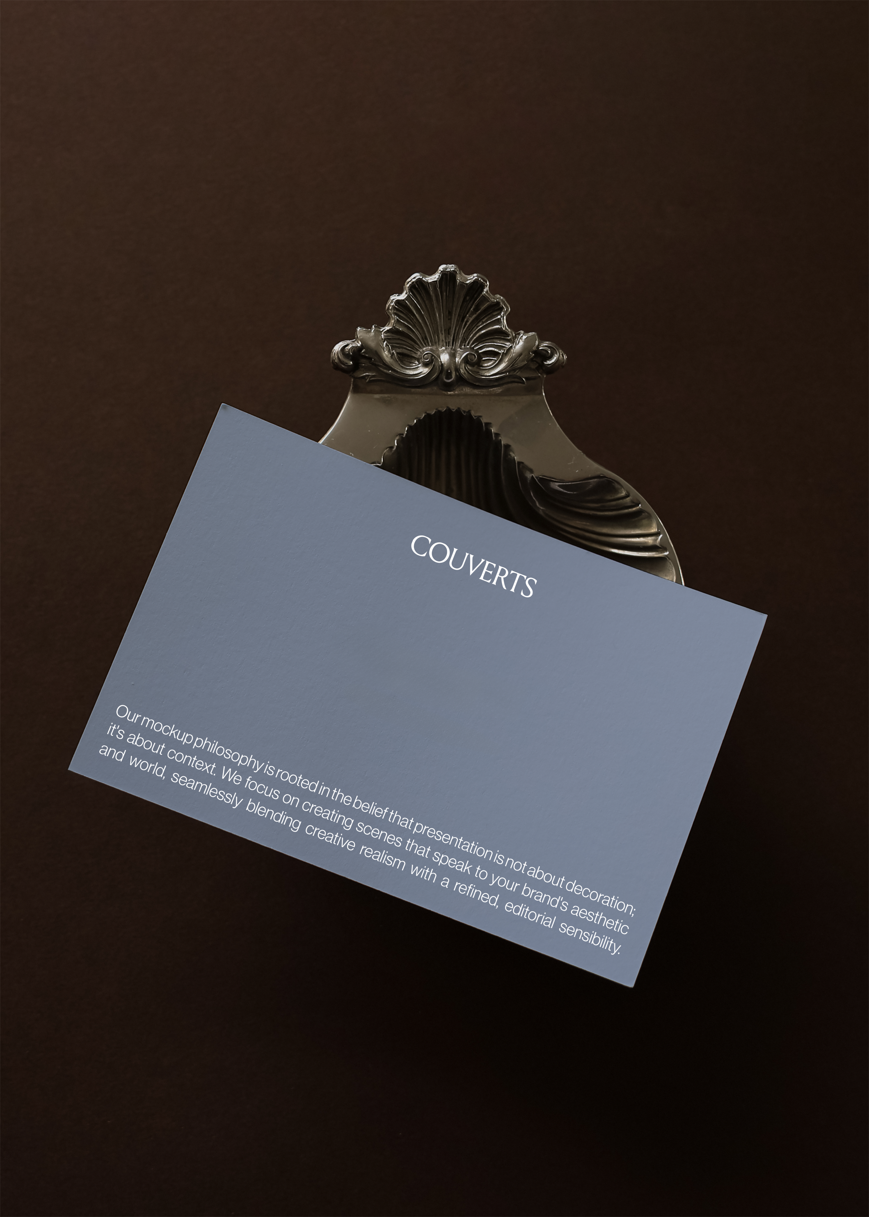 Landscape card mockup tilted against ornate silver shell clip on deep brown backdrop, candid vintage styling