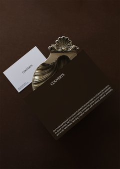 Business card and card mockup set angled together beneath ornate silver shell clip on dark brown backdrop