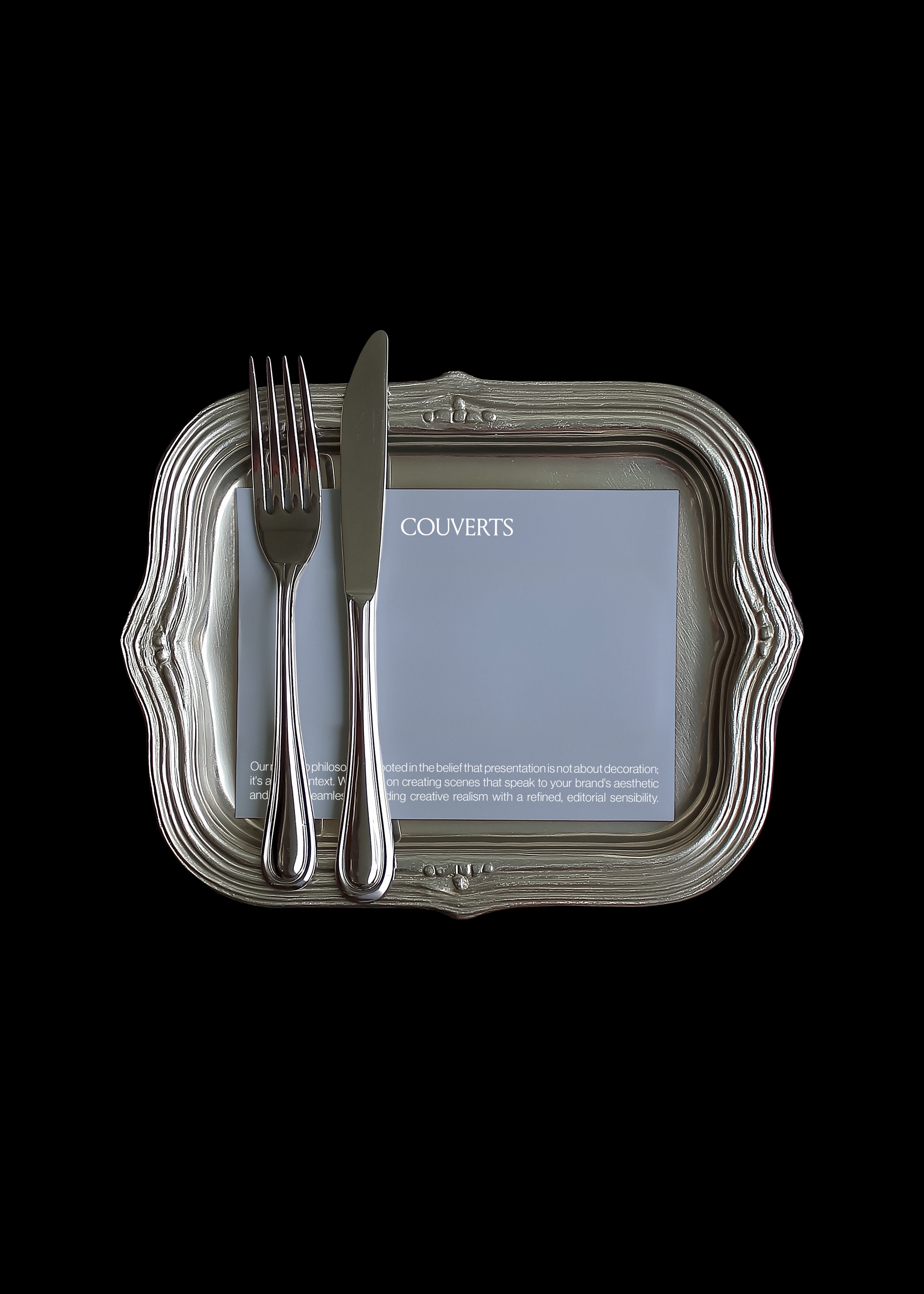 Square card mockup on ornate antique silver tray with polished fork and knife laid diagonally across the card, black background