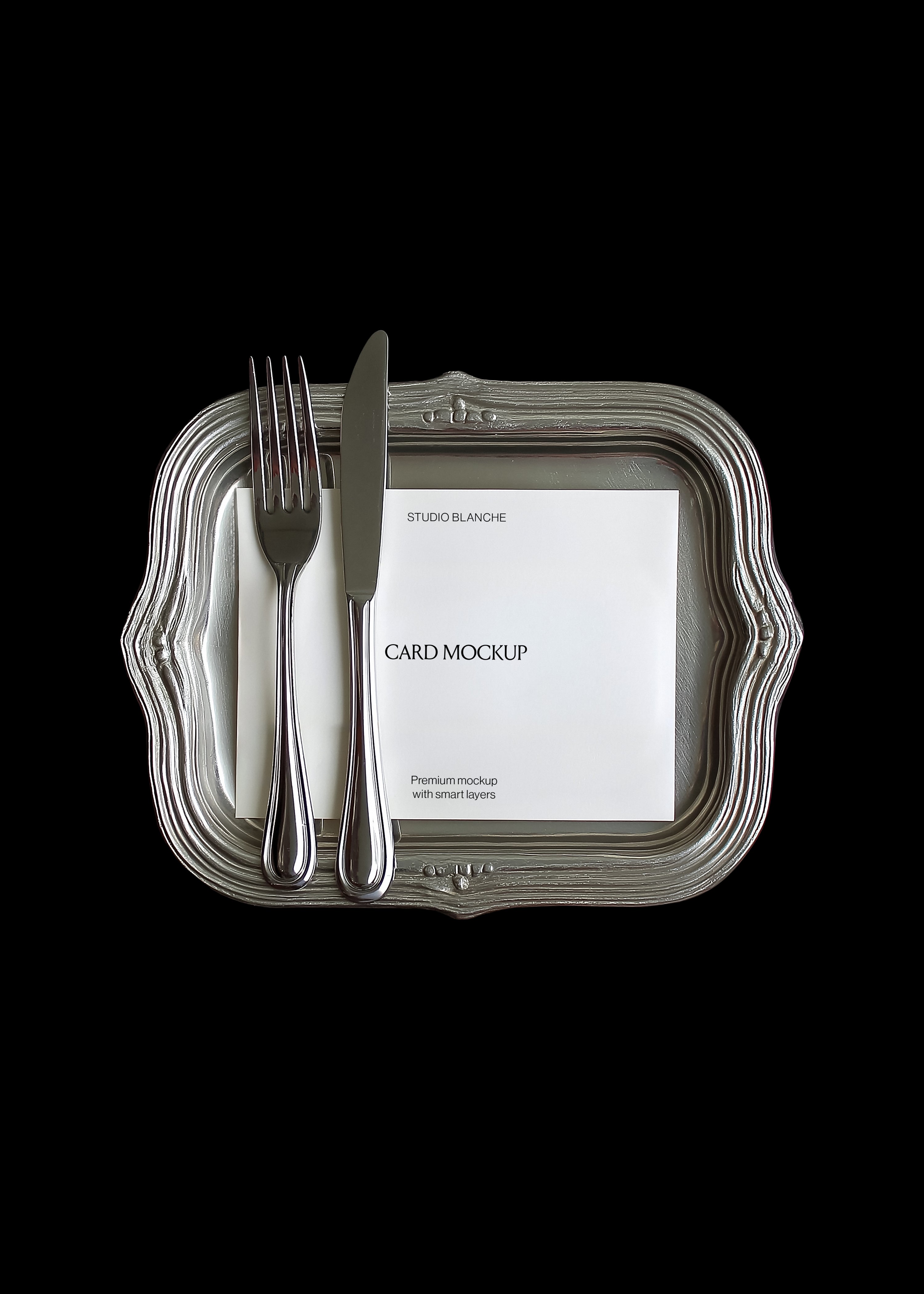 Card mockup detail on vintage silver tray showing fork and knife placement, white card with dark text, black background, top view