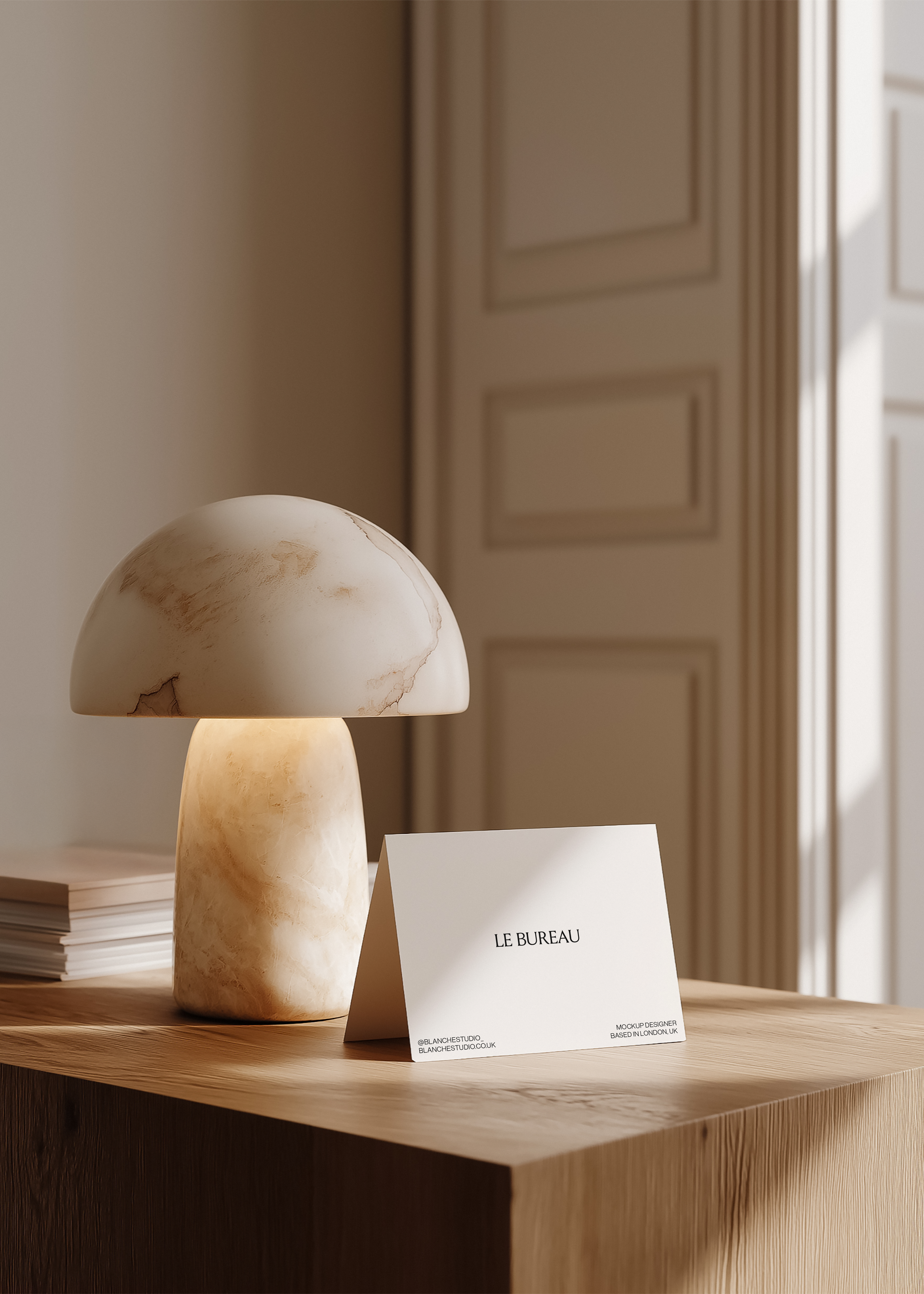 Folded card mockup displaying Le Bureau branding on pale ash console beside alabaster mushroom lamp, warm panelled interior