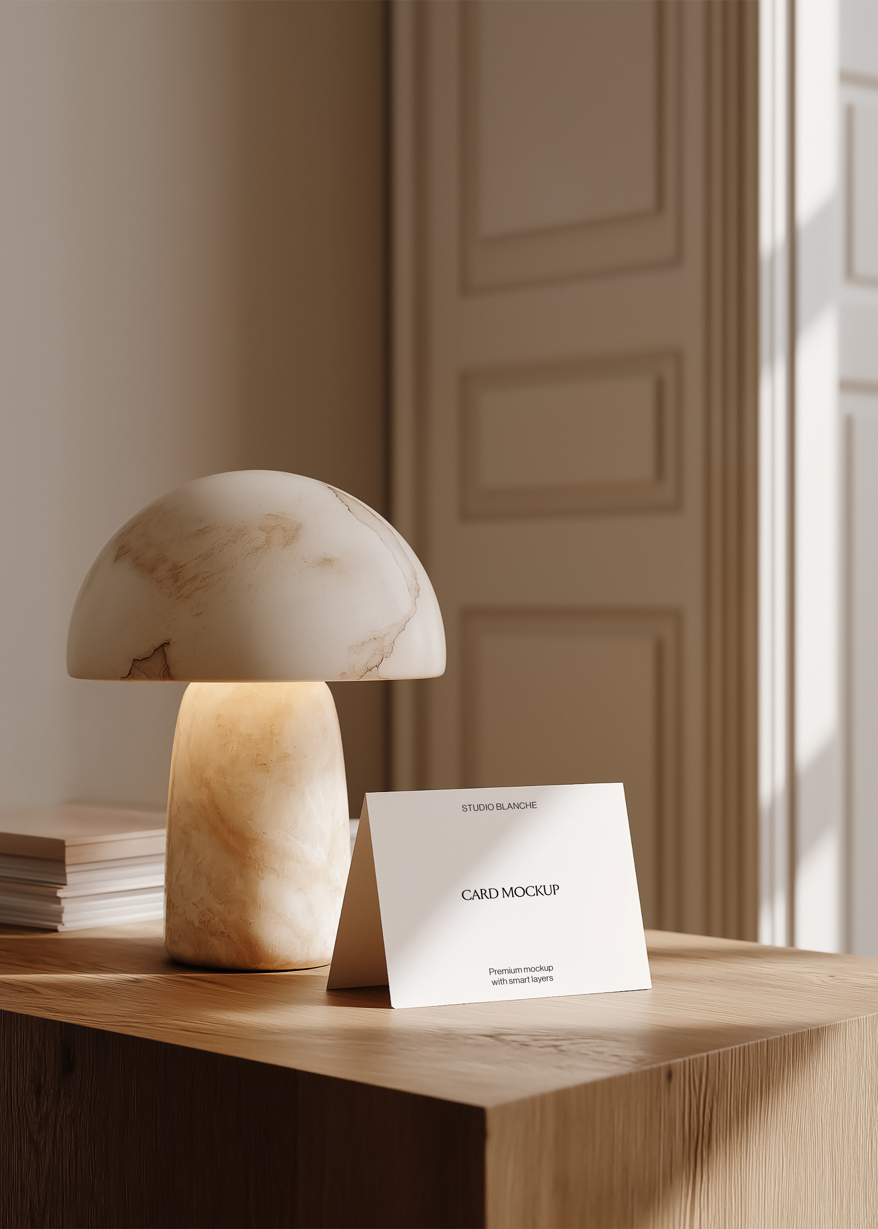 Folded card mockup propped on pale ash wood console beside veined alabaster mushroom lamp, moulded panelling and doorway backdrop 